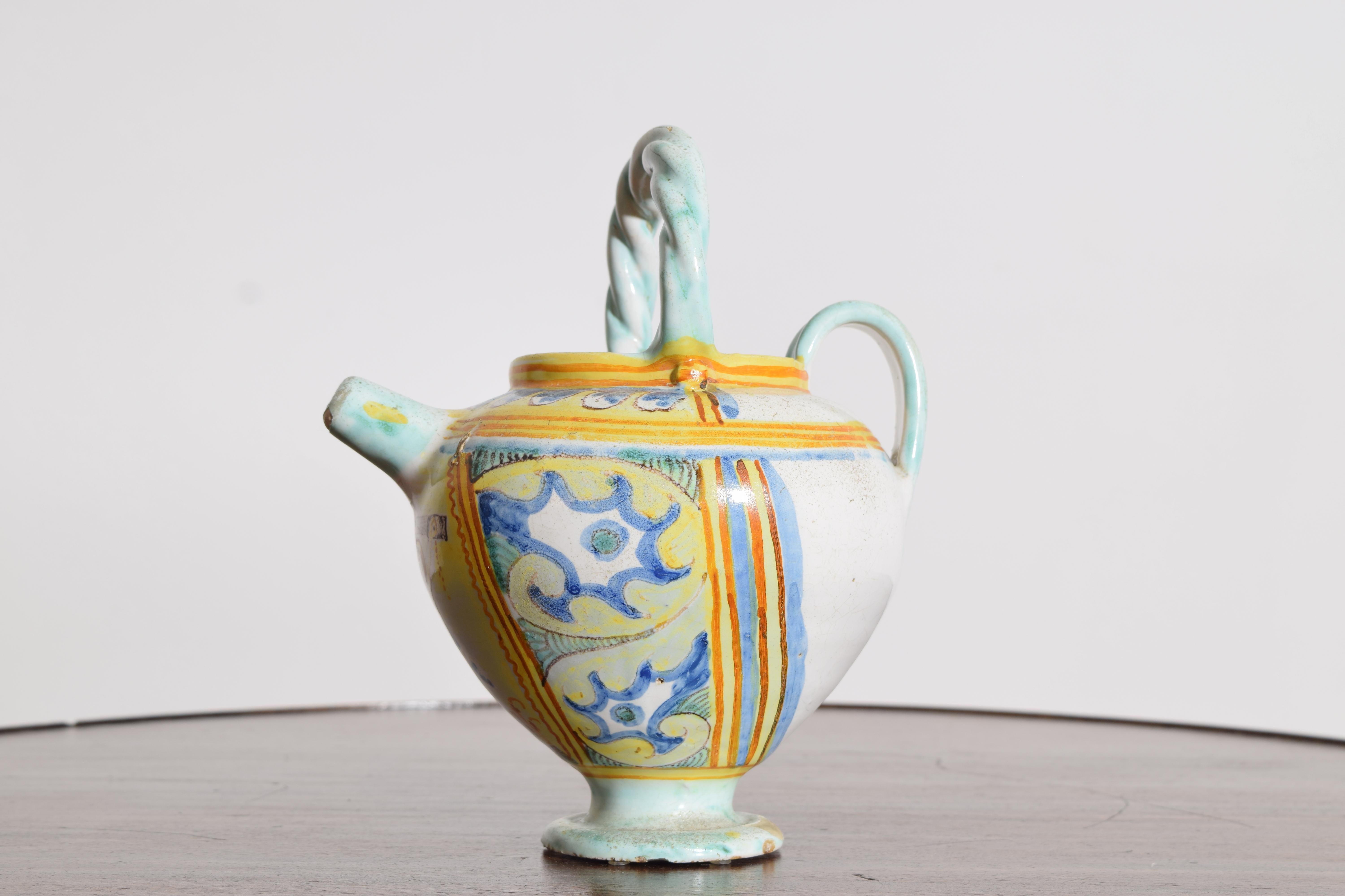 Vaso in terracotta e stagno lavorato a mano con un corpo globoso su un piede rialzato, un beccuccio corto e un manico ad arco ritorto.  Decorato con smalti maiolici policromi di colore giallo, cobalto, turchese e terracotta che alternano pannelli e