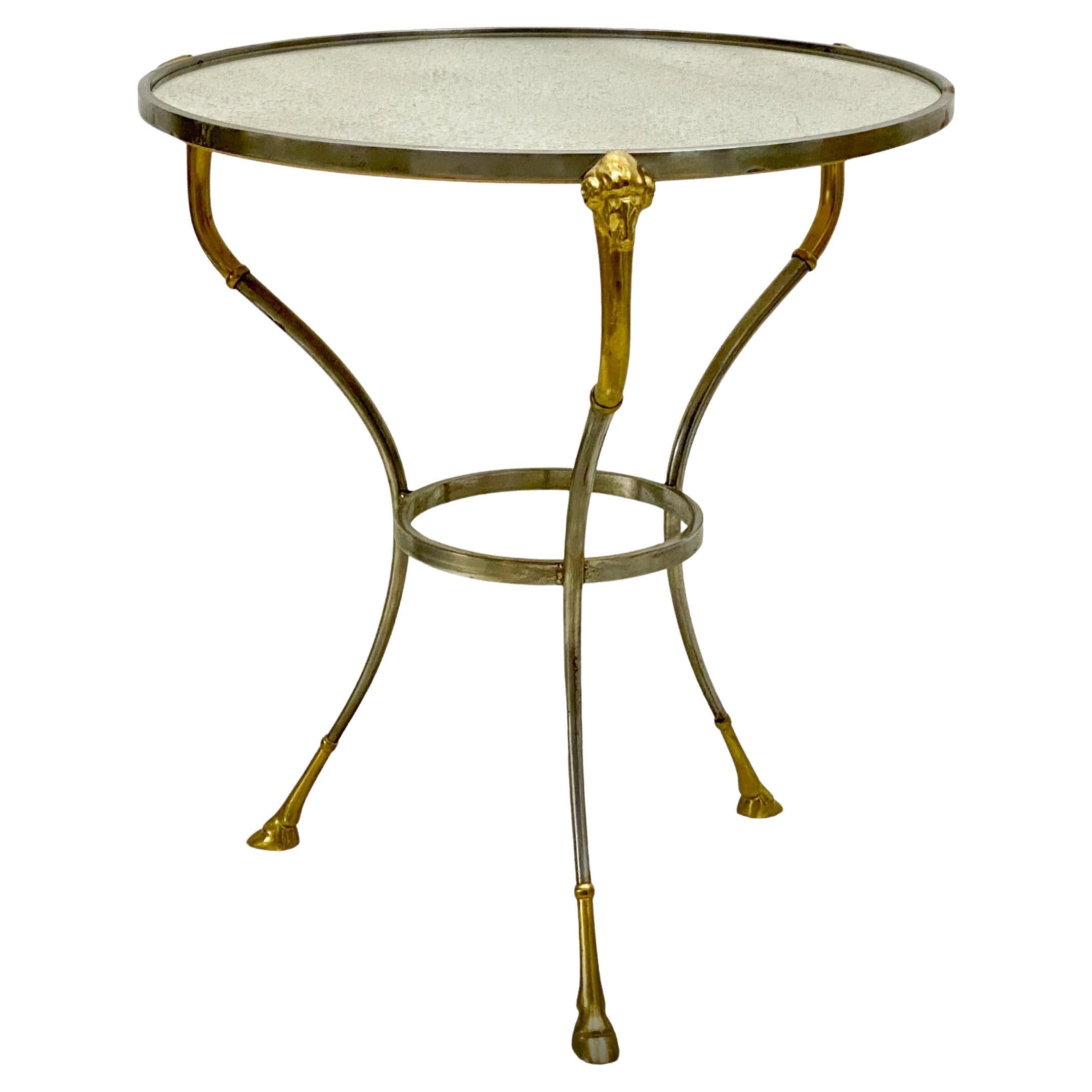 This is a 1970s Italian Maison Jansen inspired gueridon with a distressed mirrored top. The frame is steel with brass rams and hooves. It is in very good condition.