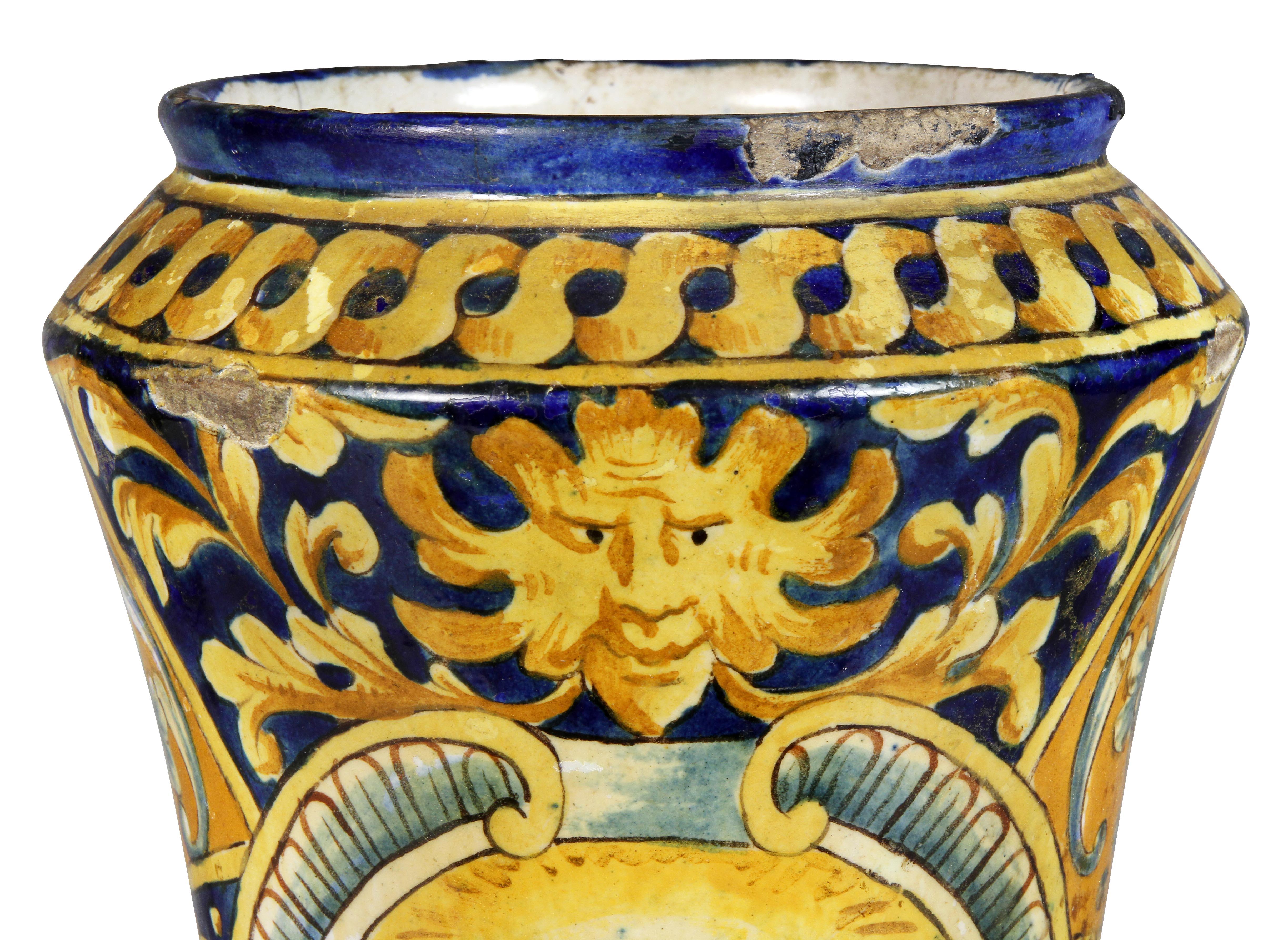 Cylindrical with concave sides and circular base. Decorated with a figure of a Roman within a cartouche, decorated overall with geometric design with scrolling leaves.