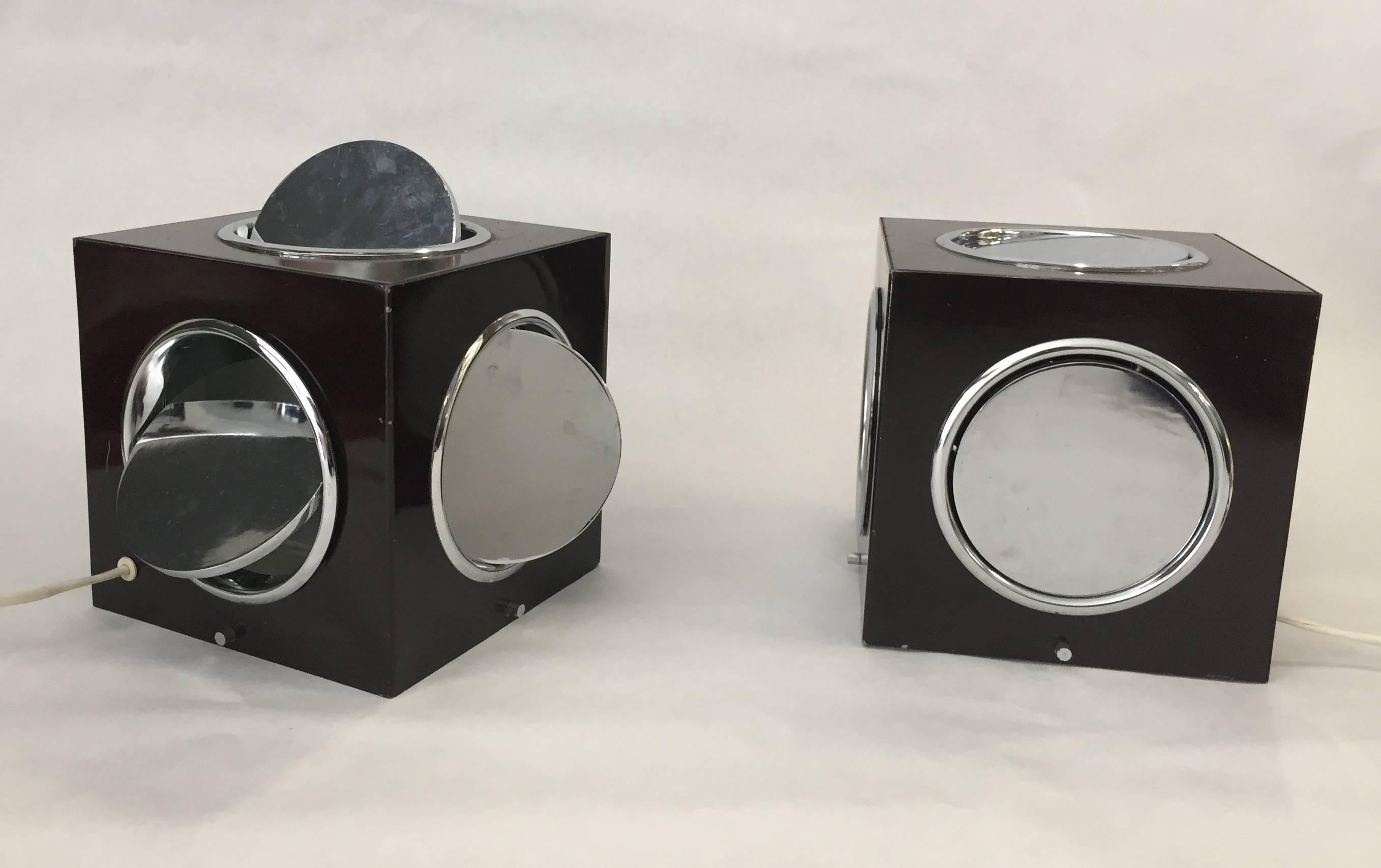 Two brown varnished metal cubical lamps. Five of the sides are open with circular portholes closed by hinged chromed metal circular windows. The portholes can be opened and the light pointed in the desired direction, that comes from a light bulb