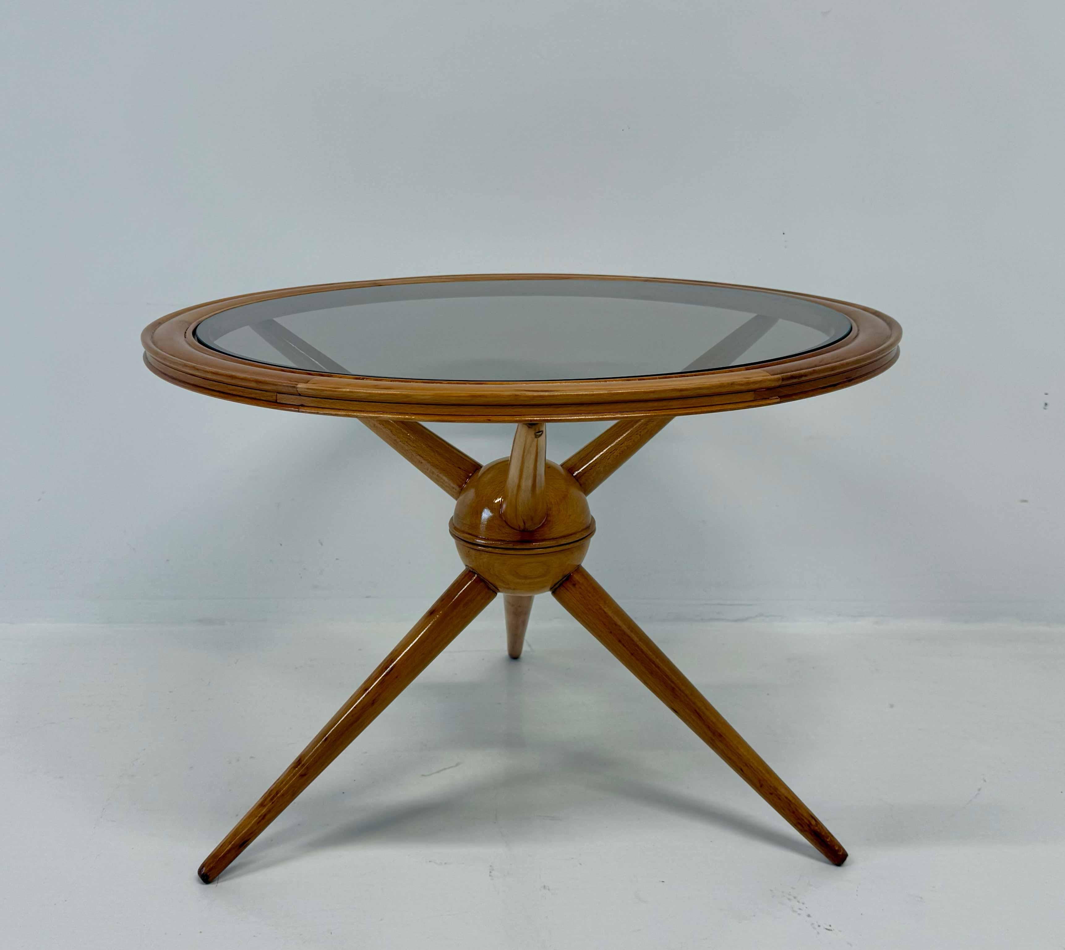 Elegant Italian coffee table crafted in the 1950s in light maple, featuring a smoked glass top and three tapered legs connected by a central wooden sphere.
The graceful silhouette and refined proportions echo the aesthetic of Cesare Lacca, a leading