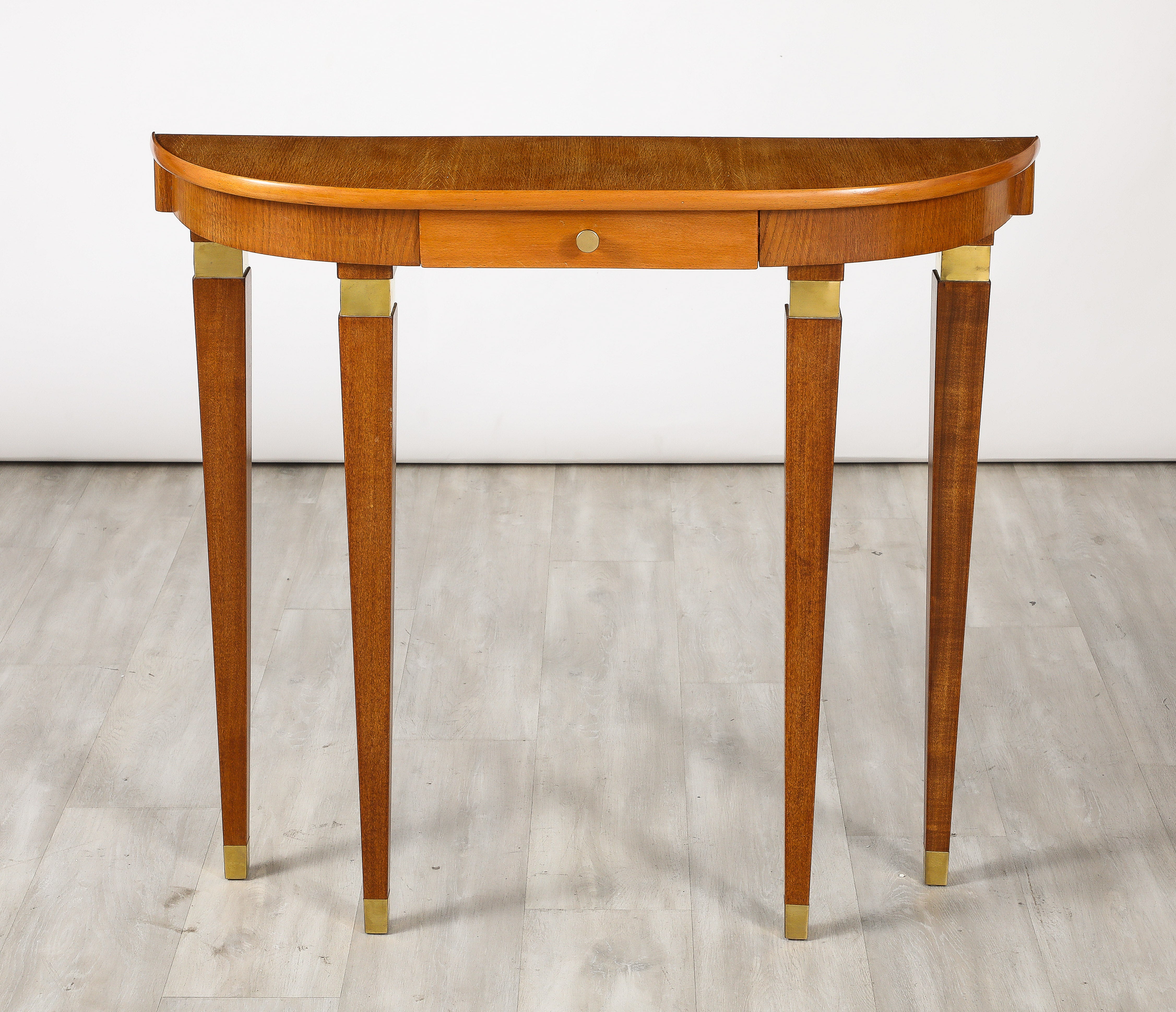 An elegantly appointed Northern Italian console table in maple.  The graceful legs are tapered and have brass banding at the top of each leg and end in brass sabot.  The legs support the demi-lune shaped top with a single drawer.  A very streamlined