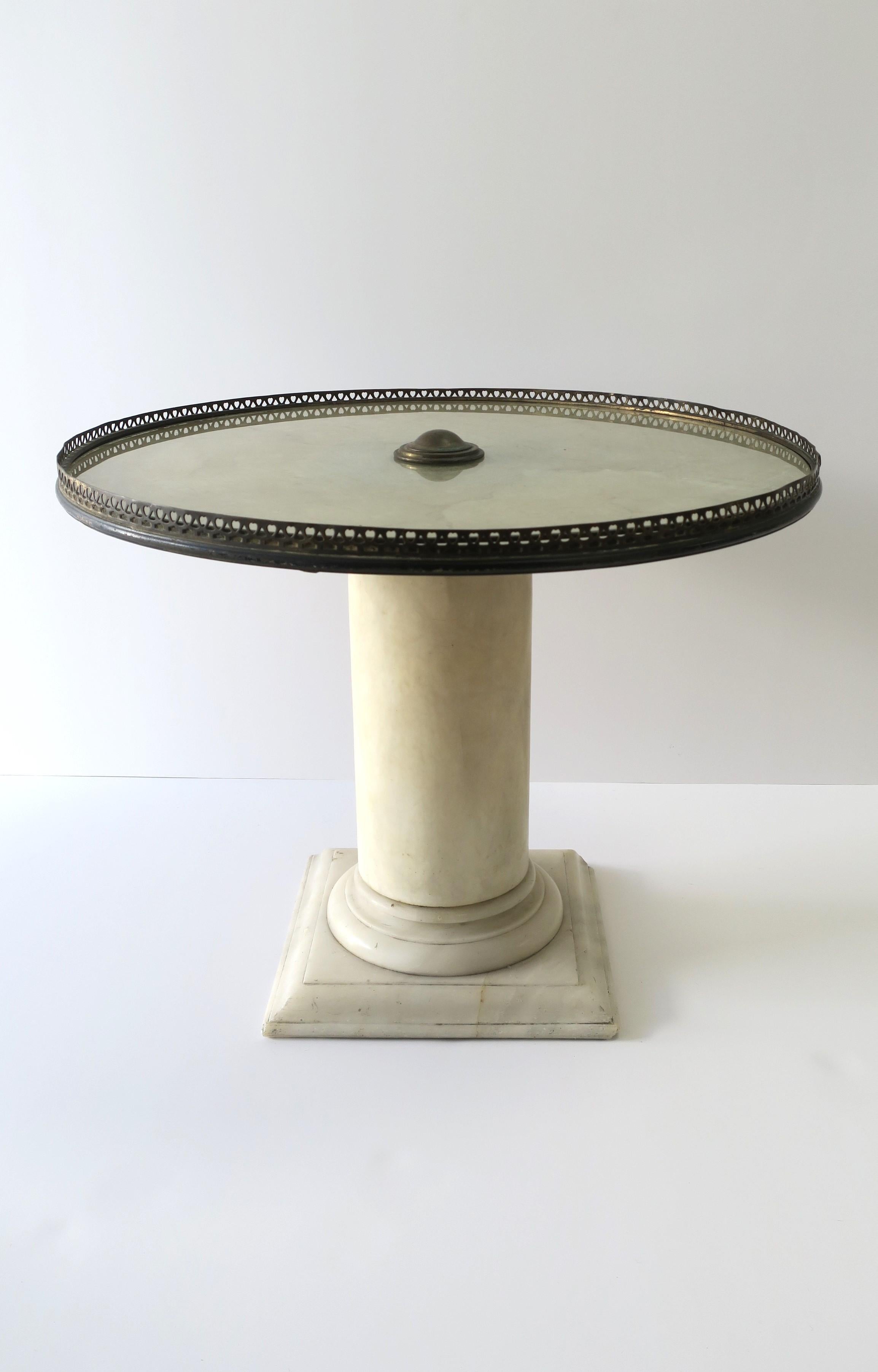 An Italian marble column side drinks cocktail table in the Neoclassical design style, circa early-20th century, Italy. Table has a solid white marble column base, glass top with a painted underside, finished with a brass knob center and perforated