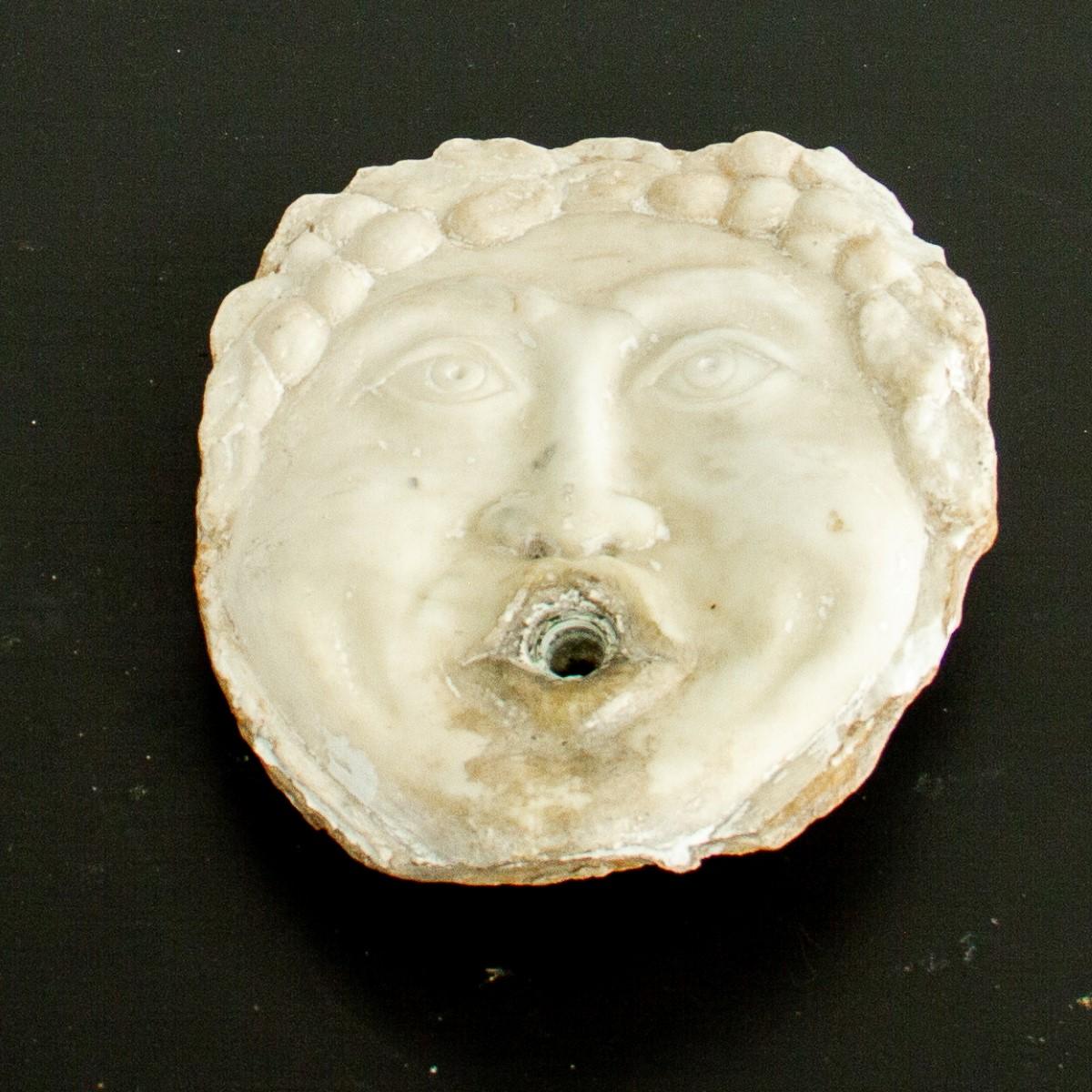 Eine italienische Brunnenmaske aus weißem Marmor, die ein männliches Gesicht mit gelocktem Haar darstellt. Diese Brunnenmasken wurden für die Aufstellung an der Wand oder auf einem Sockel über einem Becken entworfen, wobei das Wasser durch den Mund
