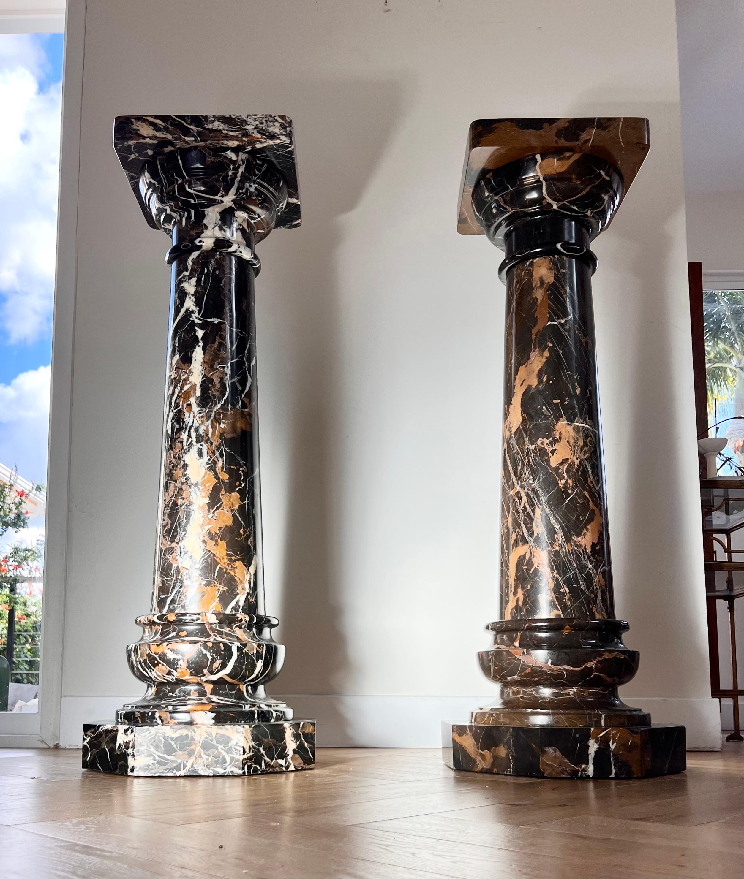 A pair of monumental vintage Italian marble pedestals, late 20th century. One pedestal is black with variegated cream and caramel veining; the other is a deep espresso hue with toffee veining. One small loss beneath the top of the first pedestal