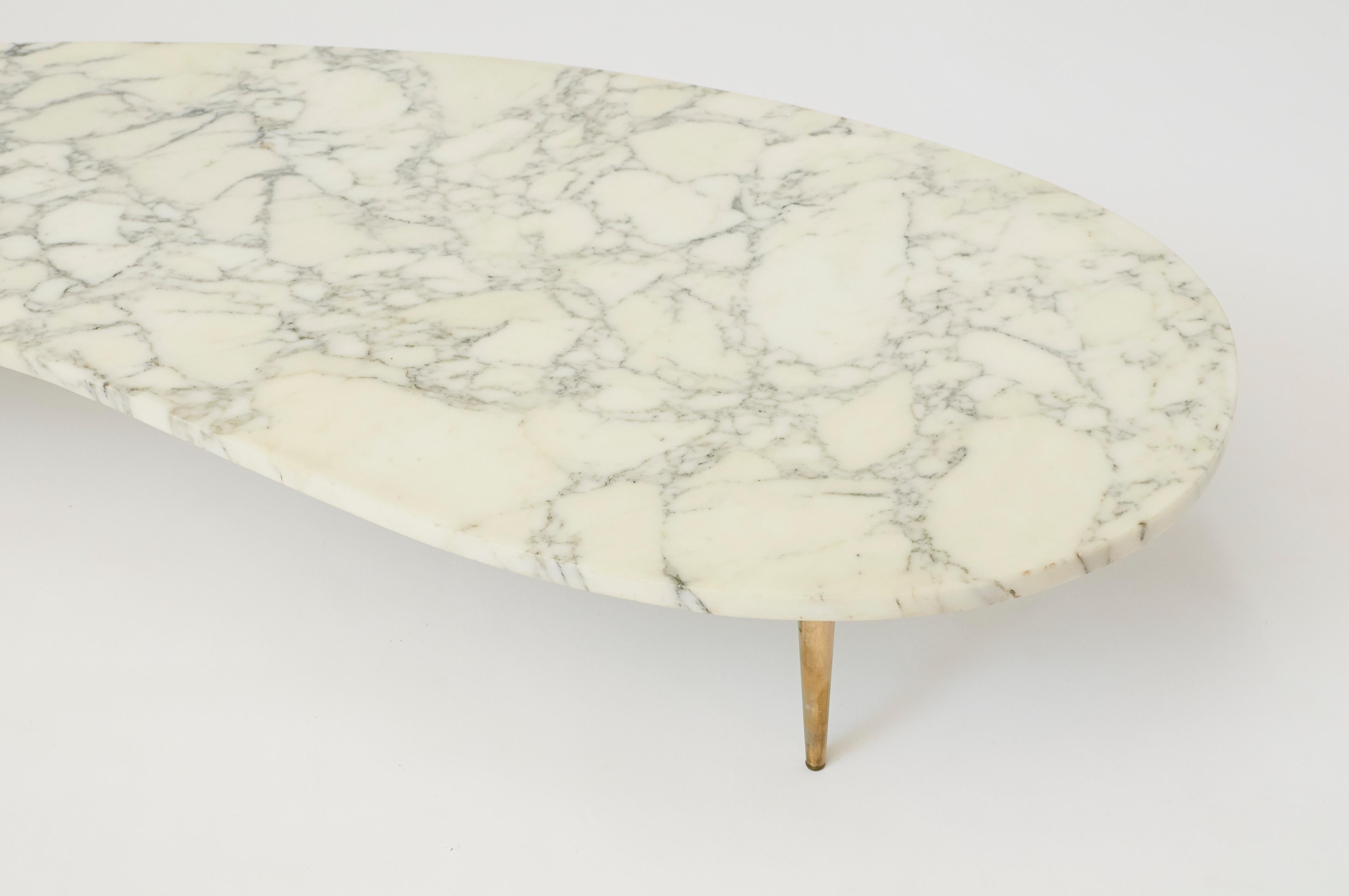 An Italian marble top coffee table with a kidney shaped top and three tapered brass legs.