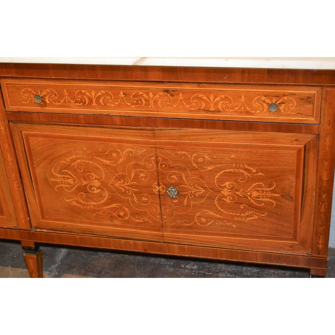 Fine quality early 20th century Italian mahogany credenza or sideboard with a white marble top. Fitted with two long drawers and two large cupboards. Exquisite satinwood marquetry inlays overall of stylized vines, leaves, and fleur de lis. The