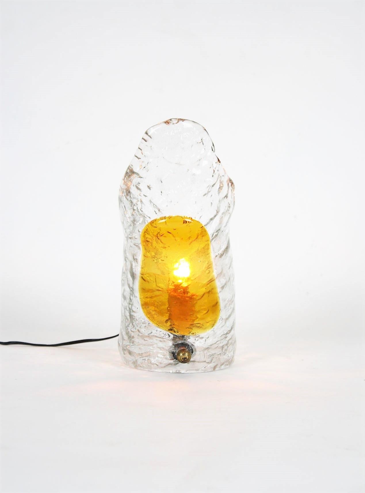 Hand blown Murano glass table lamp manufactured by Mazzega, Italy, 1960s.
Amber and Clear textured glass.
This beautiful lamp features an standing up shade with amber glass applied to clear textured glass. It has a brass ball finial as decorative