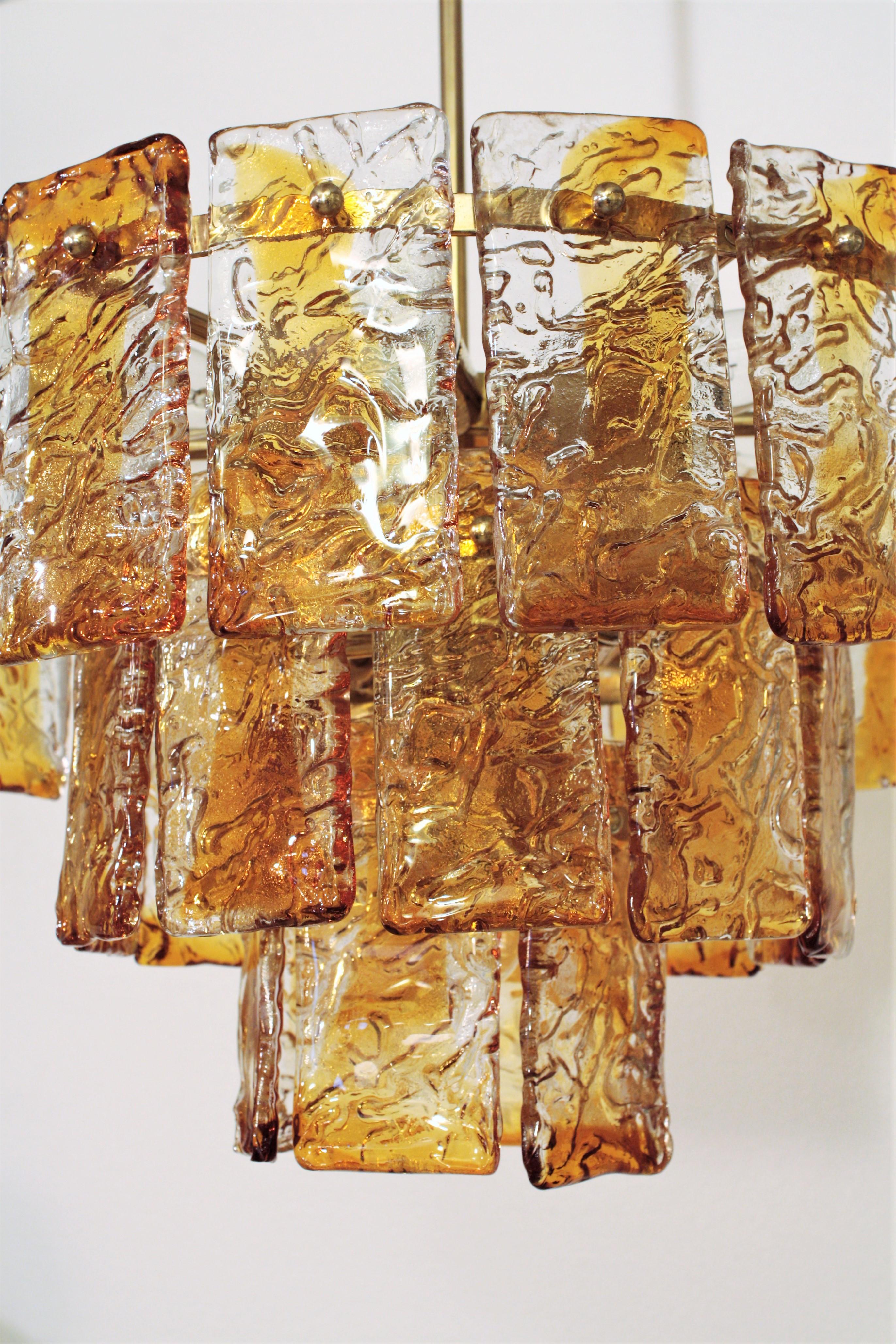 Kaskaden-Kronleuchter, Muranoglas Mazzega, Italien, 1960er Jahre
Italienischer Mid-Century Modern mundgeblasener bernsteinfarbener und klarer Kronleuchter / Pendelleuchte hergestellt in Murano von Mazzega. 
Dieser dreistöckige Kronleuchter aus