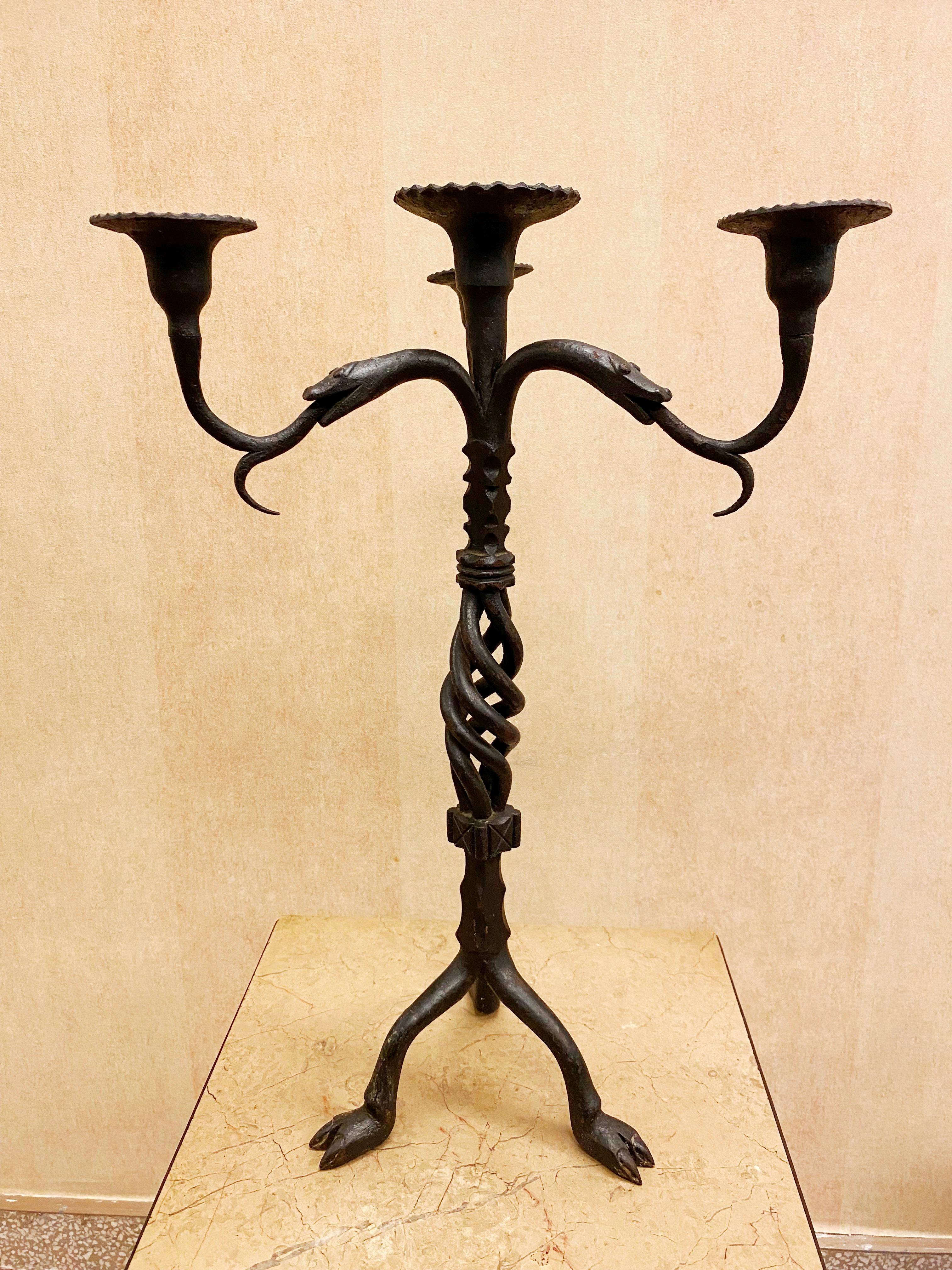 Italian Medieval Revival wrought iron candelabras with intertwined snakes, the heads holding up the drip pans with their tongues and hooved feet.