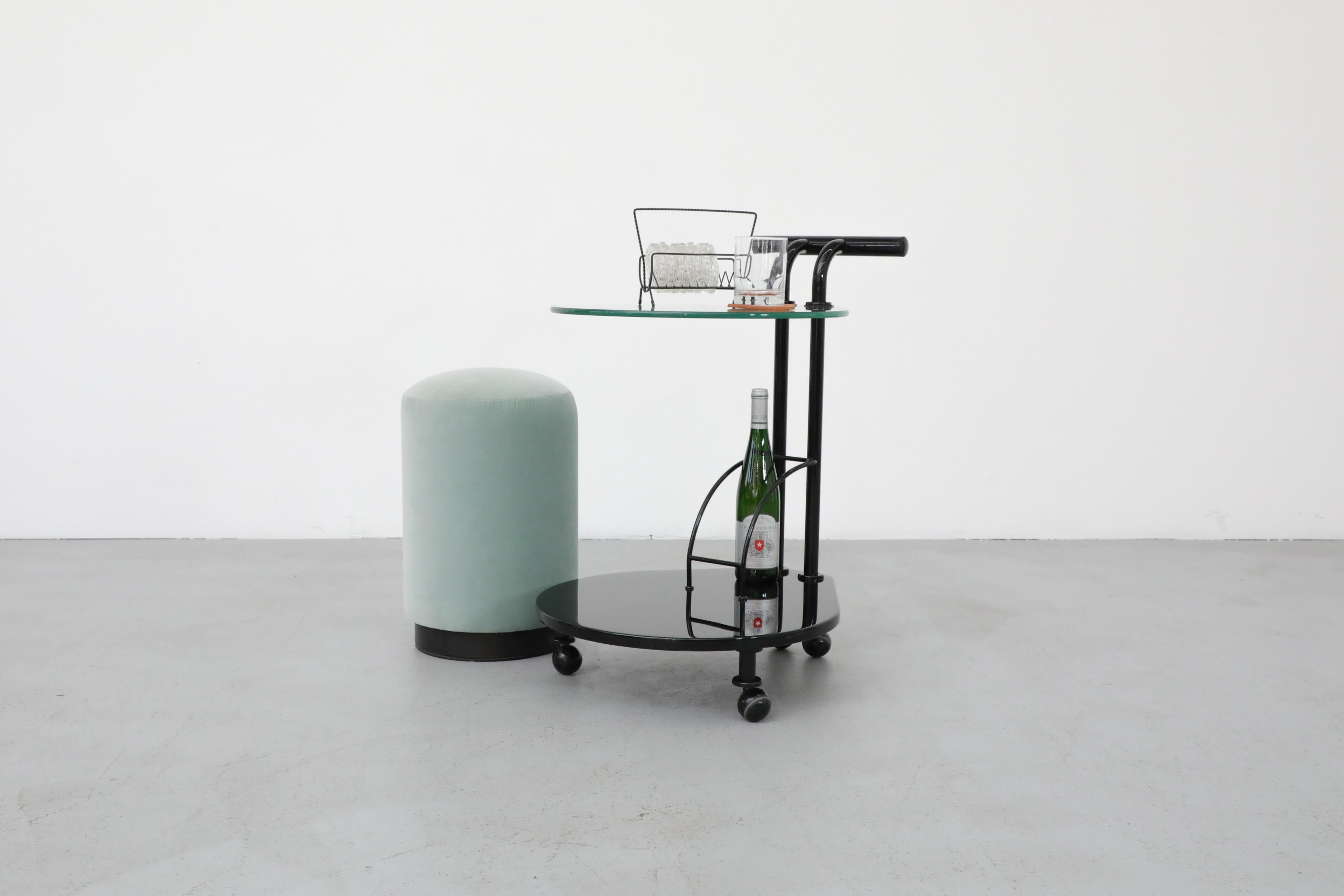 Italian Memphis style two tiered rolling bar cart with black metal frame, lacquered wood lower shelf and glass top shelf. In original condition with visible wear consistent with its age and use.