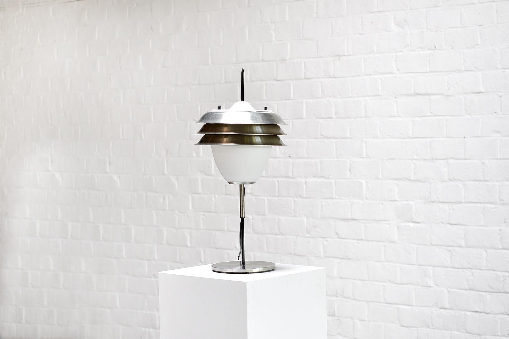 Cette lampe vintage italienne des années 1960 présente une base en acier satiné, une structure en métal noir et un grand verre opale avec trois abat-jours en métal. Un savoir-faire exceptionnel et un design intemporel. Le concepteur nous est