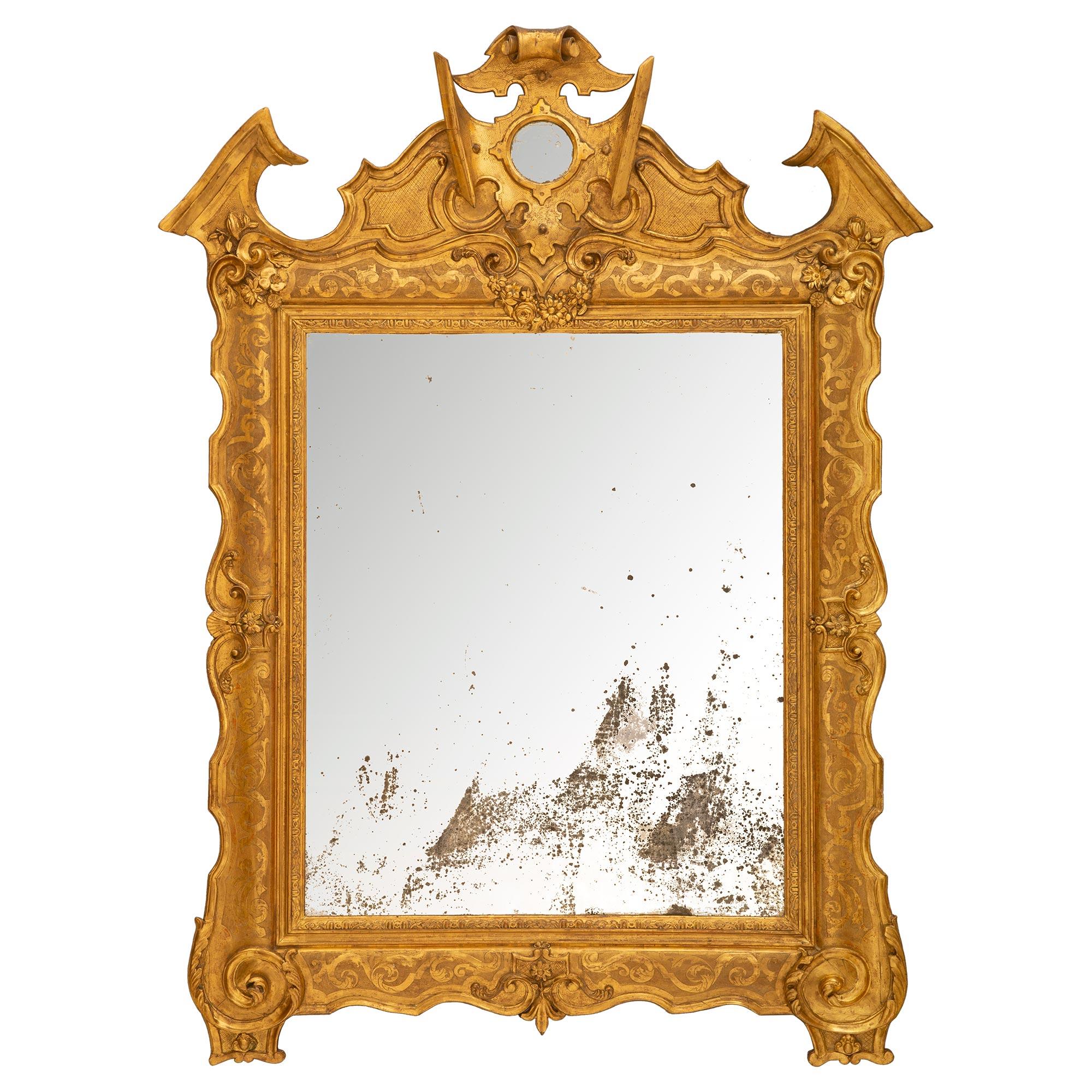A very handsome Italian mid 19th century giltwood mirror from Naples. The original mirror plate is framed within a straight carved giltwood band with charming carvings within a fabulous scalloped frame. Mottled border and exquisite interlocking