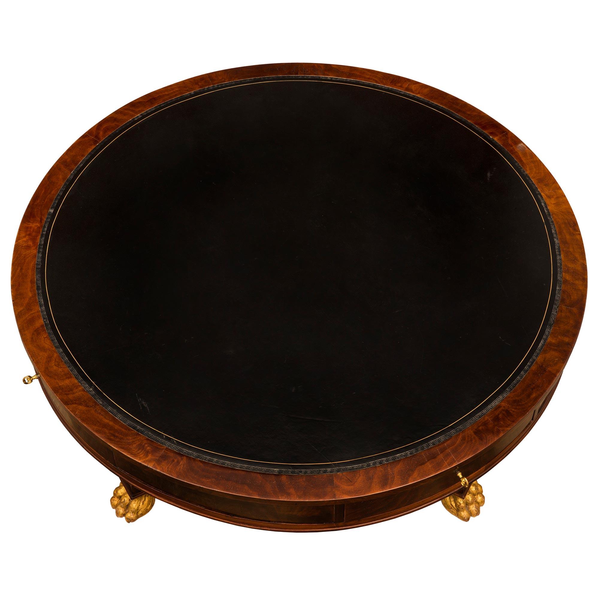 A stately and most handsome Italian 19th century Neo-Classical st. flamed Mahogany and giltwood library/center table. The four drawer circular table is raised by impressive richly carved giltwood paw feet below elegant circular fluted legs with