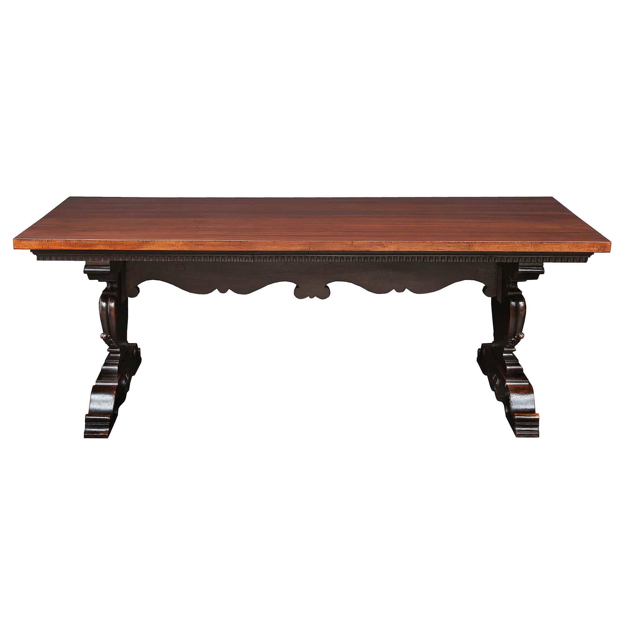 A handsome and large-scale Italian mid-19th-century solid walnut trestle table. The table is raised by extremely decorative carved supports displaying richly scrolled patterns with a floral and reeded design. At the center connecting the two