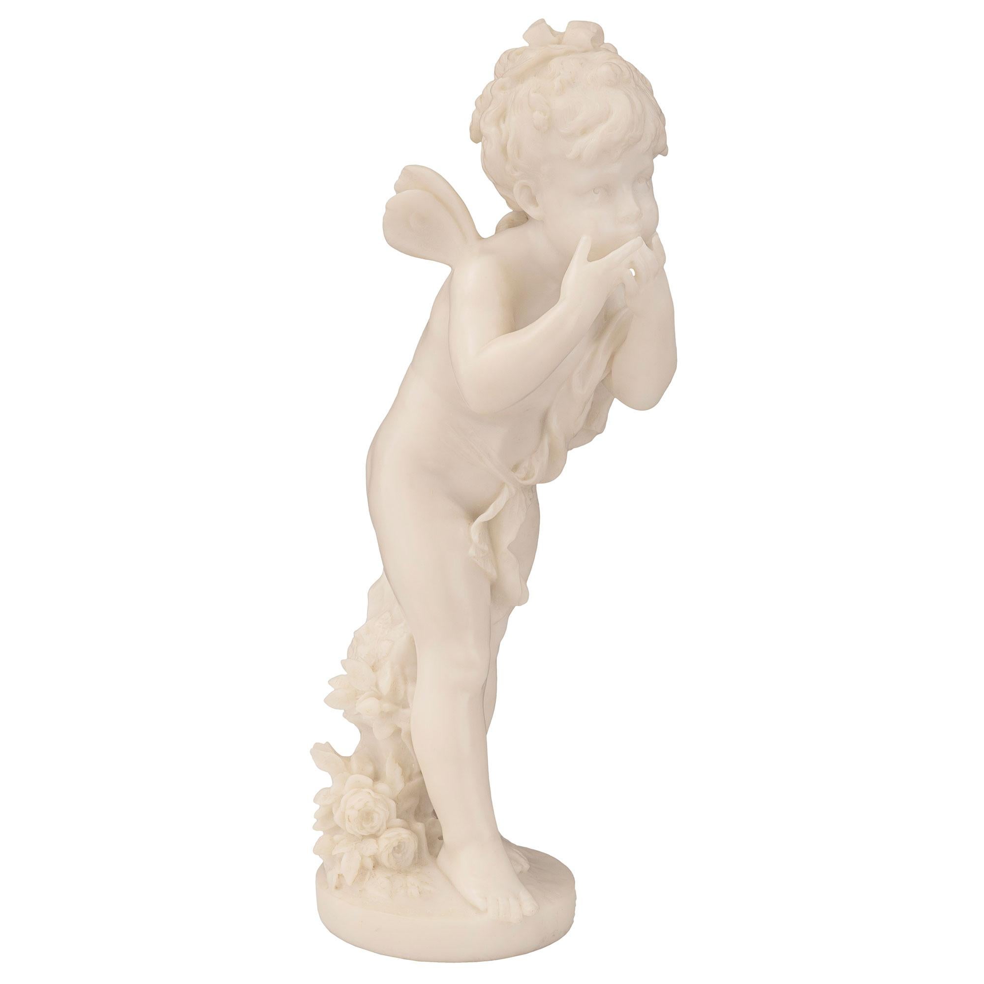 Statue de jeune fille ailée en marbre blanc de Carrare, datant du milieu du XIXe siècle, absolument charmante et bien exécutée. La jeune fille se tient au-dessus d'un socle circulaire sur lequel est posé un bouquet de fleurs richement sculpté. Elle
