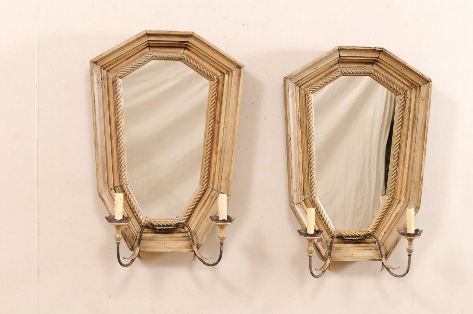 A nicely-sized Italian pair of two-light sconces with mirrored back-plate from the mid-20th century. This pair of vintage scones from Italy each feature a large shied-shaped back-plate consisting of a wood frame with roped carved inner surround