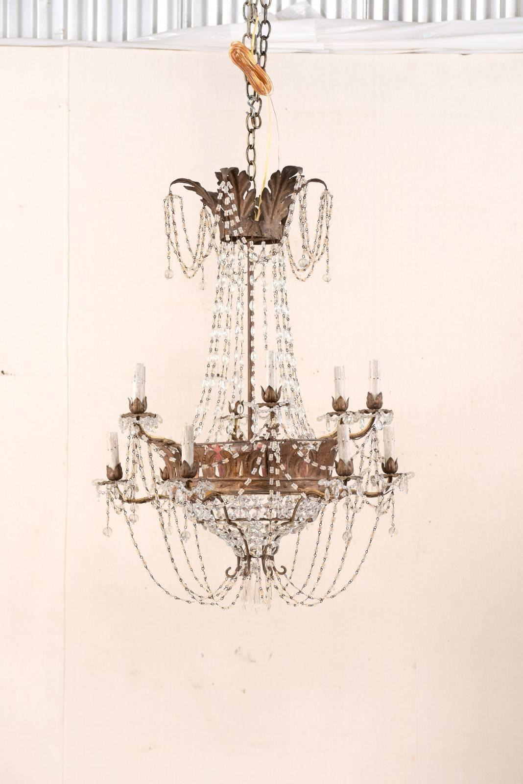 An Italian midcentury twelve-light crystal basket chandelier. This antique chandelier from Italy features a two-tiered, basket design with anthemia decorated crown and gallery. Harmonious swags of crystal and Italian glass beads are draped