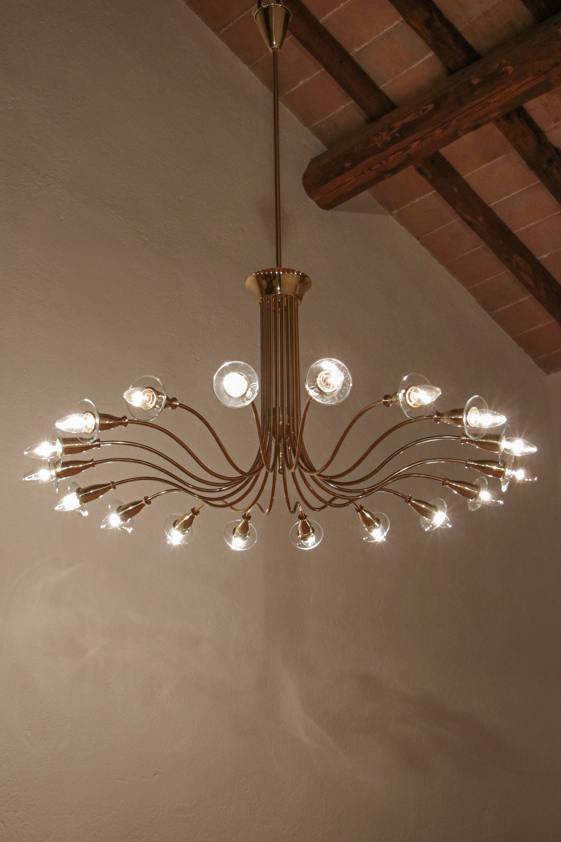 Magnifico lampadario disegnato da Angelo Lelli per Arteluce nel 1950. Realizzato in ottone lucido con vetri molati, questo lampadario presenta diciotto luci di formato E14. Il design di grande impatto scenico si unisce a una qualità esecutiva