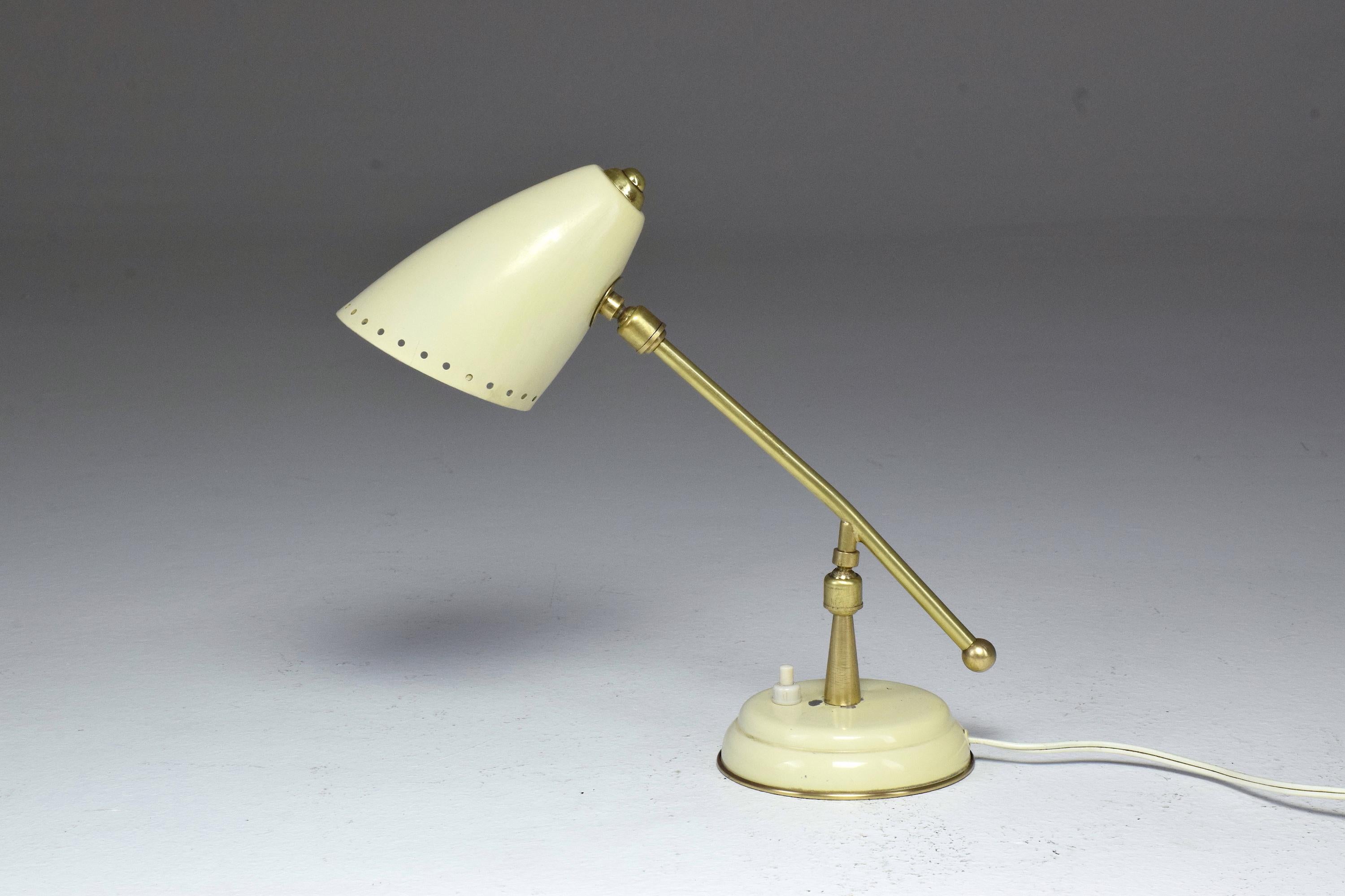A 20th century vintage Italian table or desk lamp design with a polished brass stem, double articulation and a perforated cocotte shade. The lamp adjusts in height, length and width. The shade and base are in lacquered beige aluminum and the push