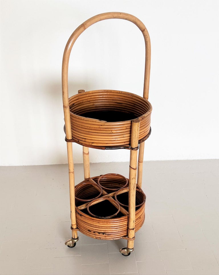 Gorgeous small bar cart or trolley made of curved bamboo and wicker during the Italian mid-century in the 1960s.
The cart is circular with two tiers, long handle, and 4 rollers. 
The lower shelf has four spaces for bottles.
The four rollers are