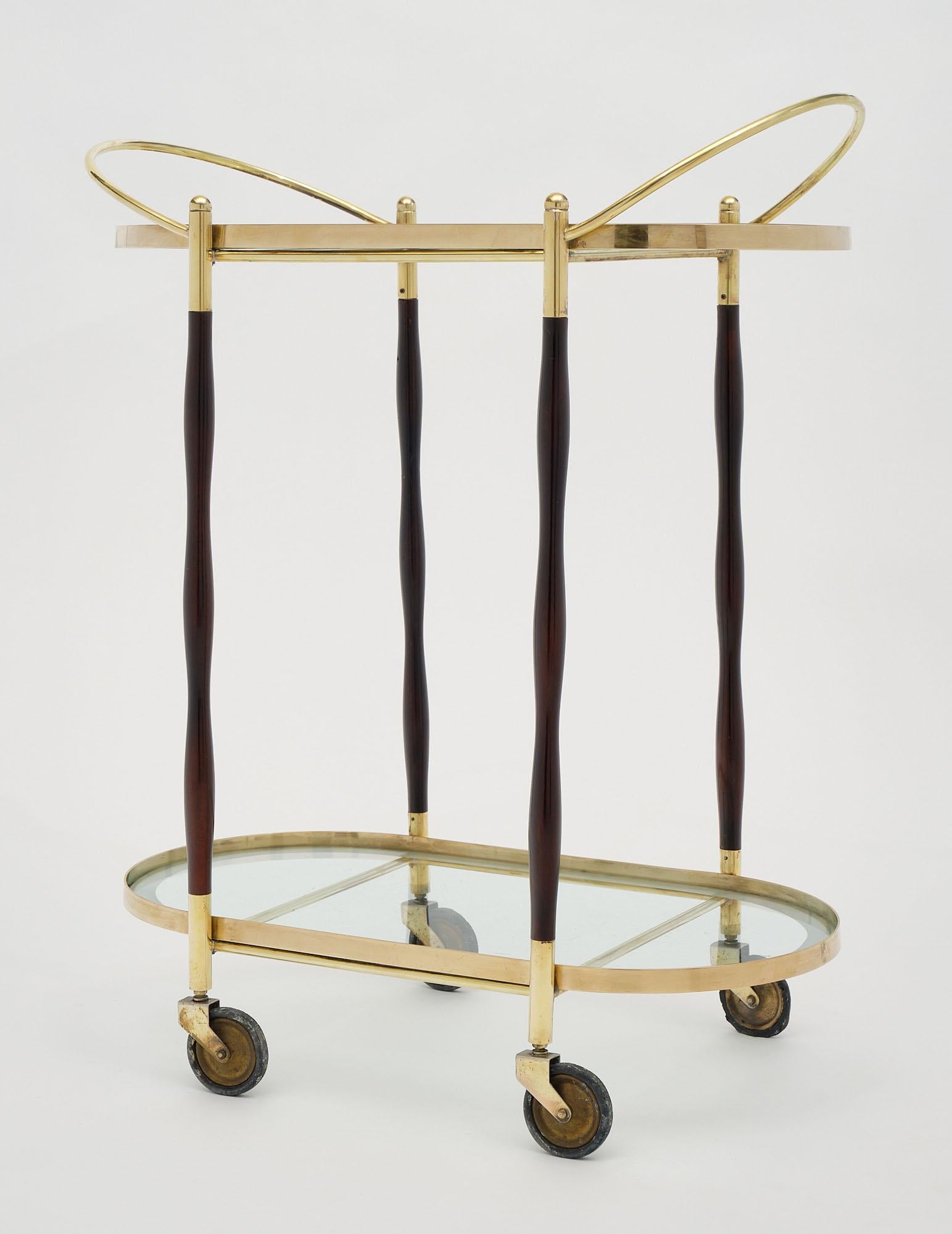 Bar cart from Italy from the Art Deco period made of solid polished brass and featuring two clear glass shelves with a frosted edge. There are four ebonized and French polished turned wood legs.