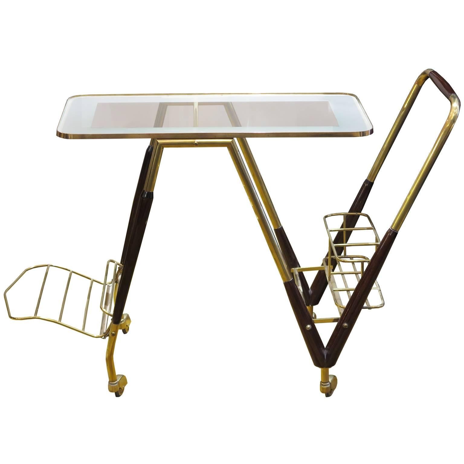Italian midcentury bar cart on wheels in brass with mahogany details. Frosted and clear glass top with a brass rim. Bottle holder and magazine rack in brass attached to frame.