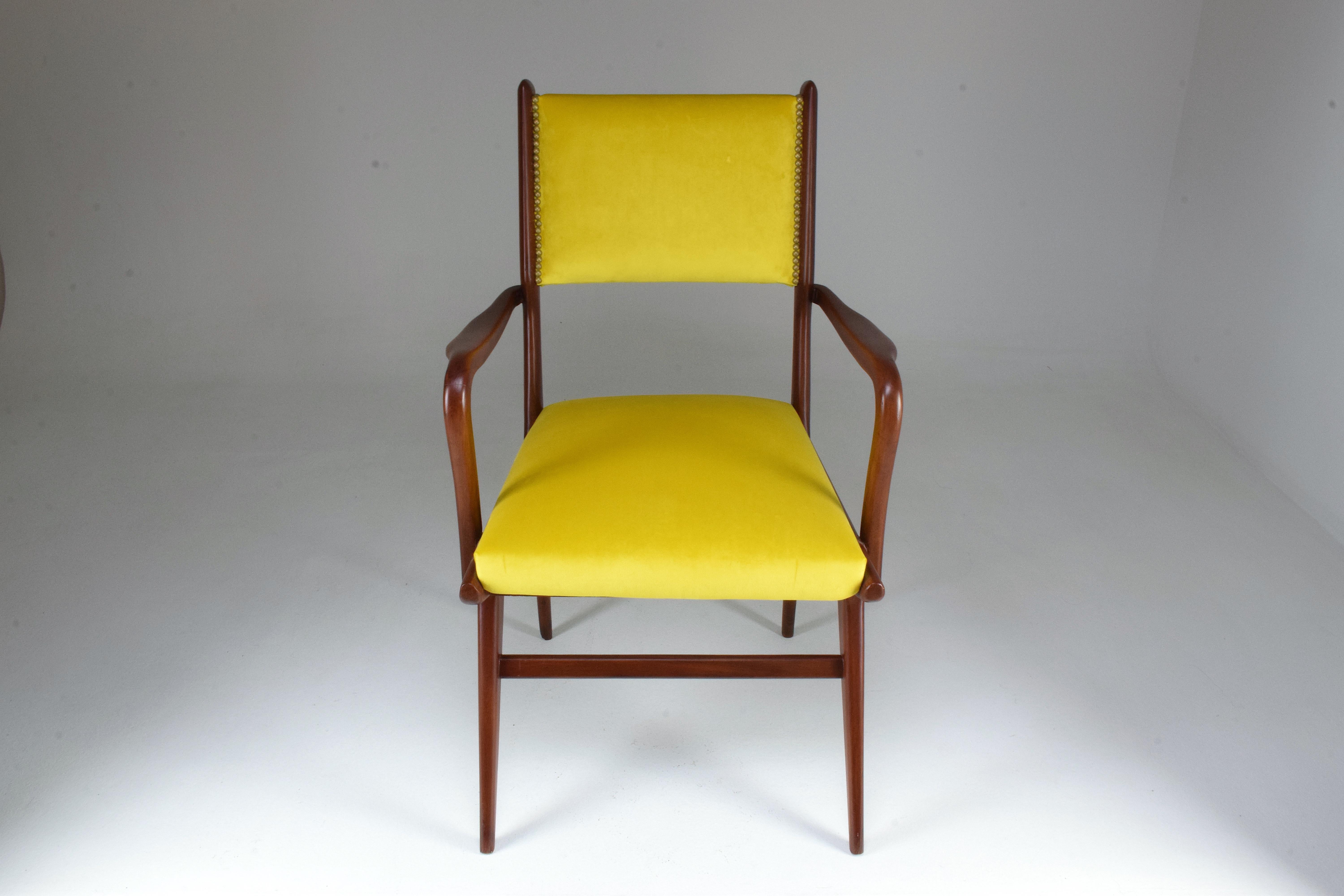 A 20th century vintage Italian armchair designed with curved armrests and splayed and tapered front legs with stretchers. This design piece is fully restored with yellow velvet upholstery and nailhead trims on the front and back of the seat rest.