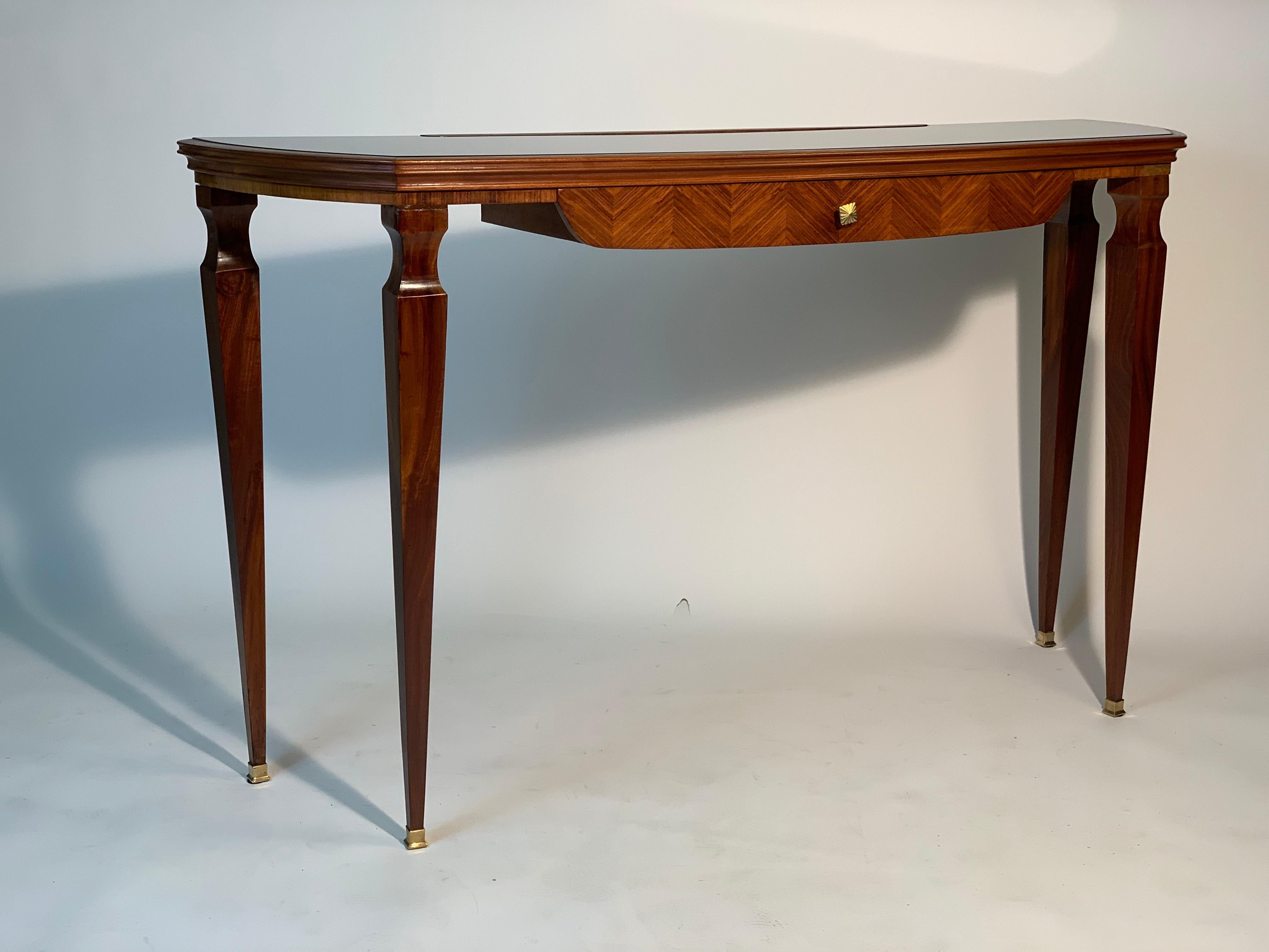 Mid-century Italian console with convex sides, black glass top, four truncated cone legs that tighten downwards and ending with four brass feet, a herringbone inlaid drawer with a precious and luxurious wood is embellished with a cast brass