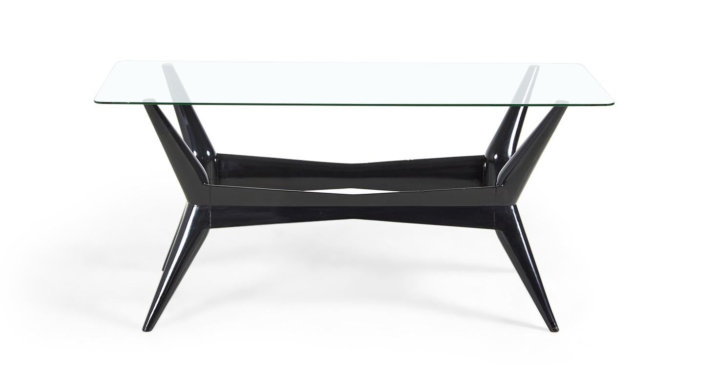 Italian mid-century black painted coffee table with tapered legs and carved edges supporting a rectangular glass top.
  