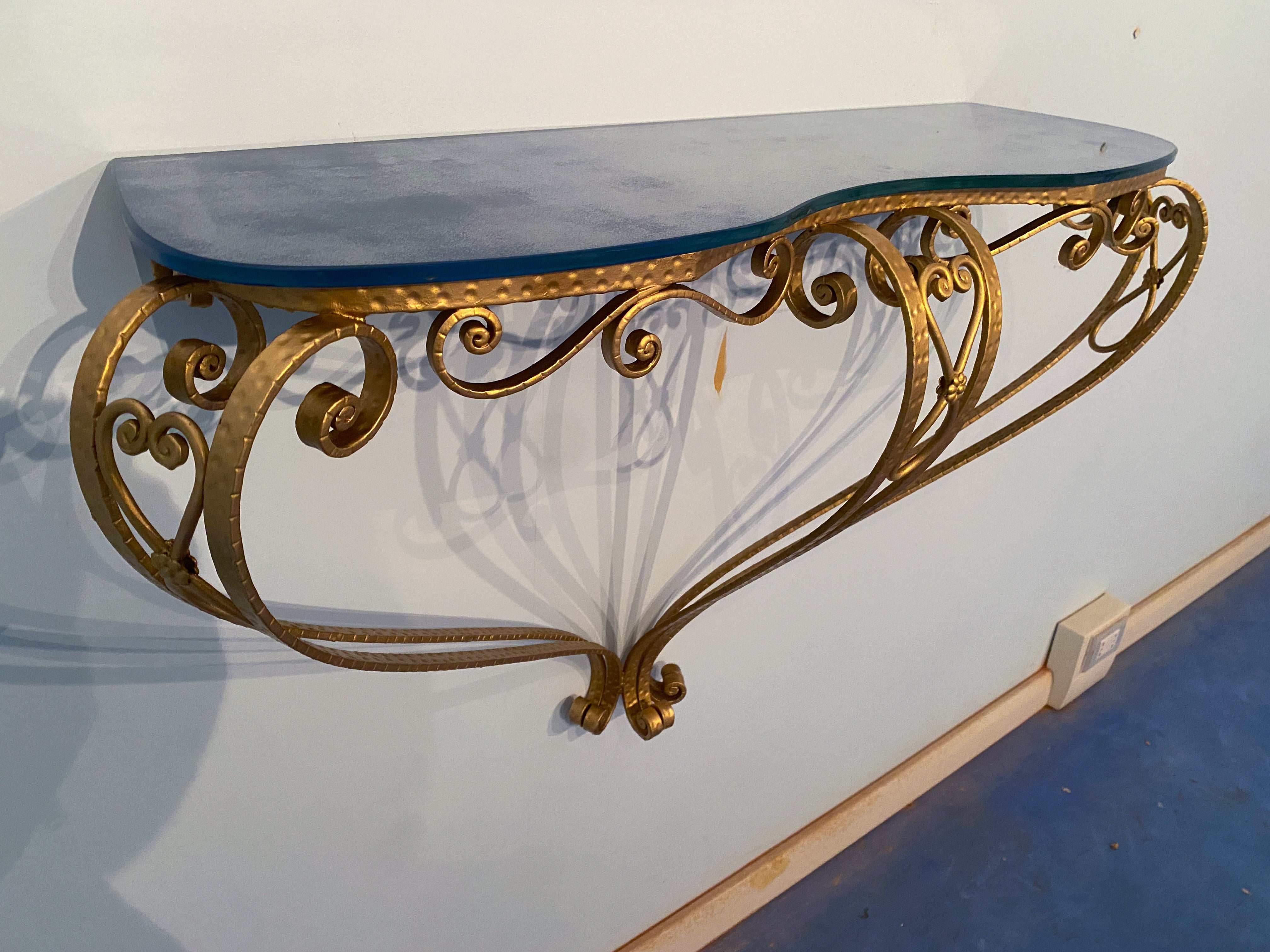 This elegant console, designed in the 1950s by Pierluigi Colli, is a true work of art that stands out for its expert handcrafted metalwork, meticulously crafted down to the smallest detail. Its sculpted blue glass top, further enriched by delicate