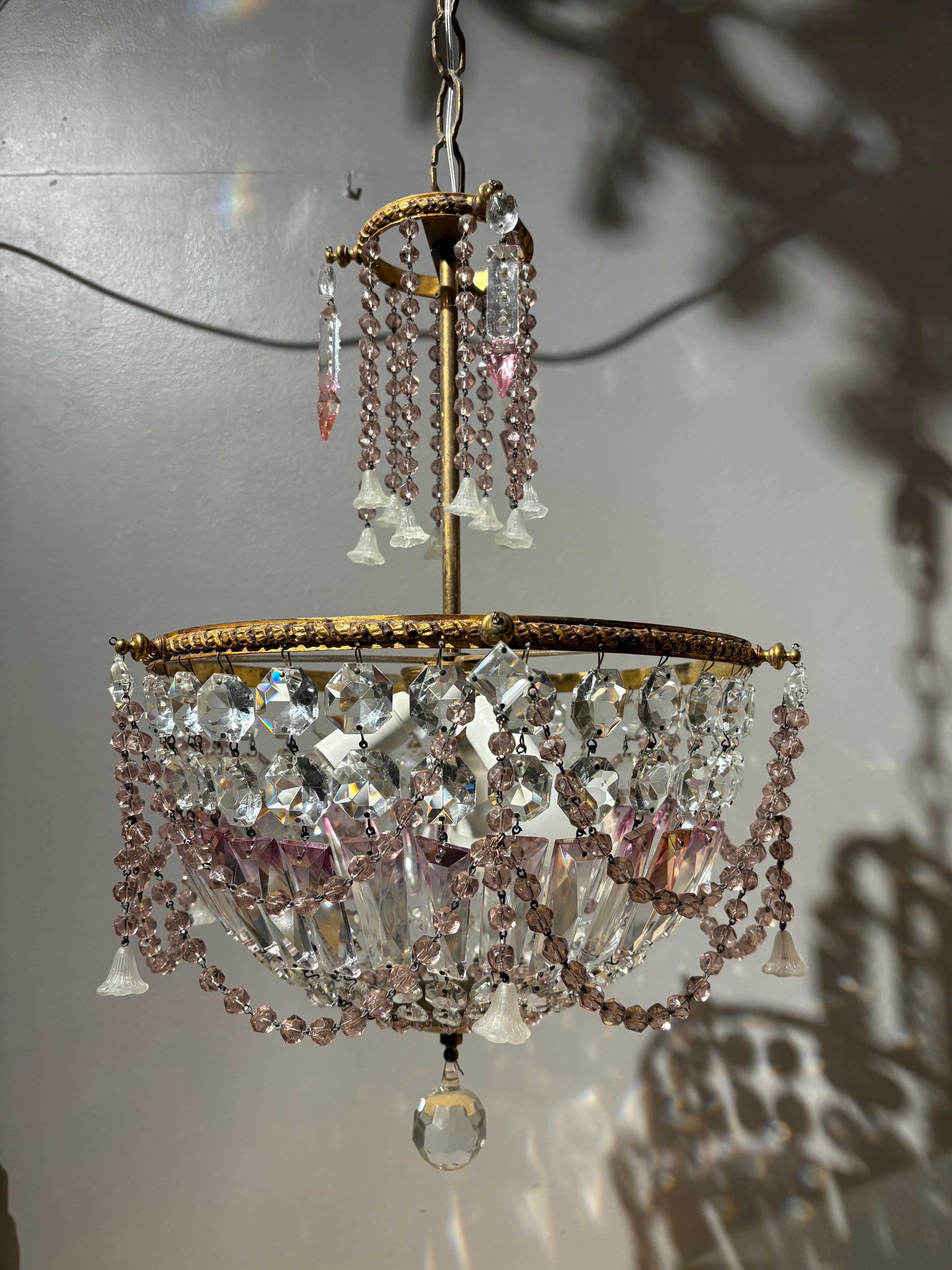 Elegante araña de los años 50 con un marco de latón bellamente detallado y adornada con prismas de cristal de Bohemia y delicadas cuentas teñidas de rosa. La araña tiene tres luces, que crean una iluminación refinada y chispeante. Las guirnaldas de