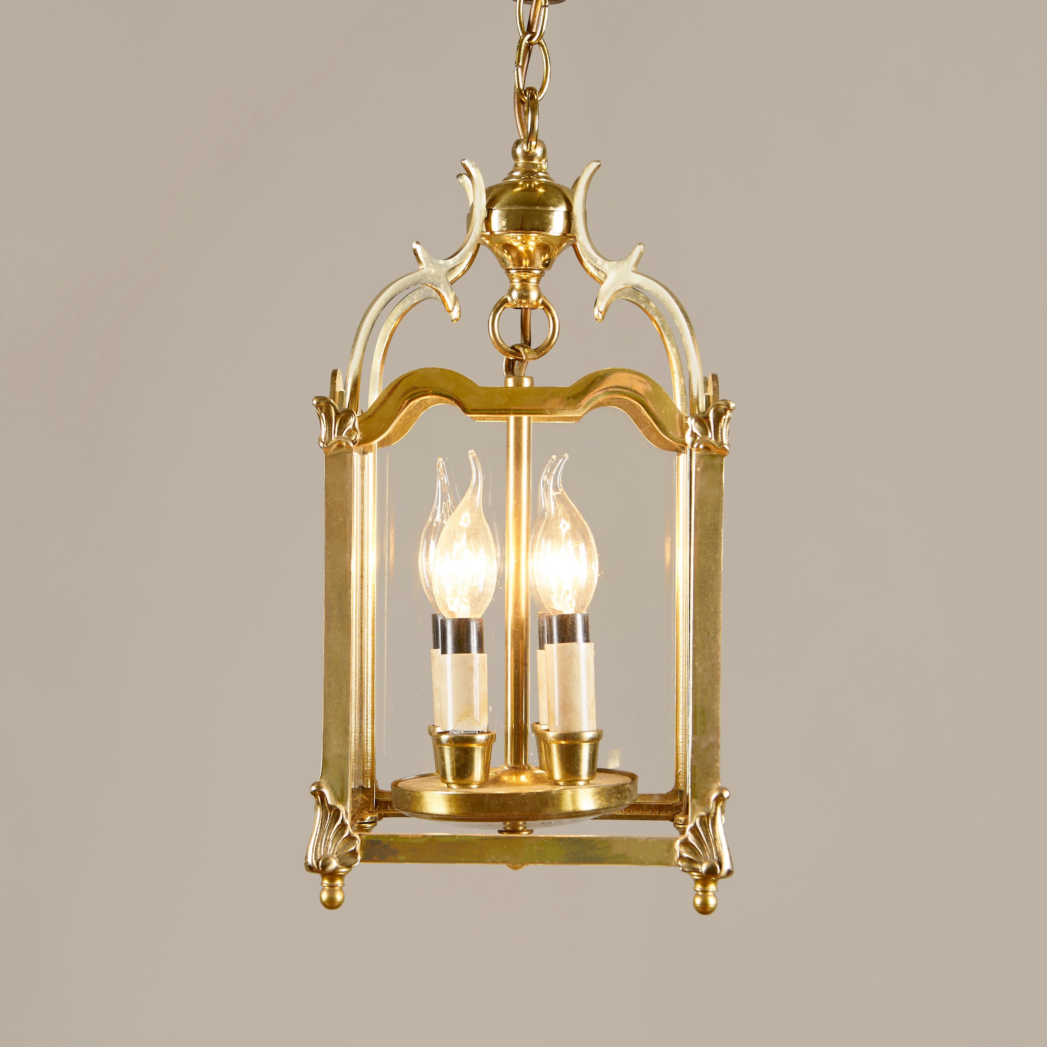 Four square glass panels supported from the top to the canopy by scrolling arms, brass shaped frame and decorative filials. A central brass hanging rod supports four interior electrified candle sleeves.
Perfect for adding a touch of glamour to the