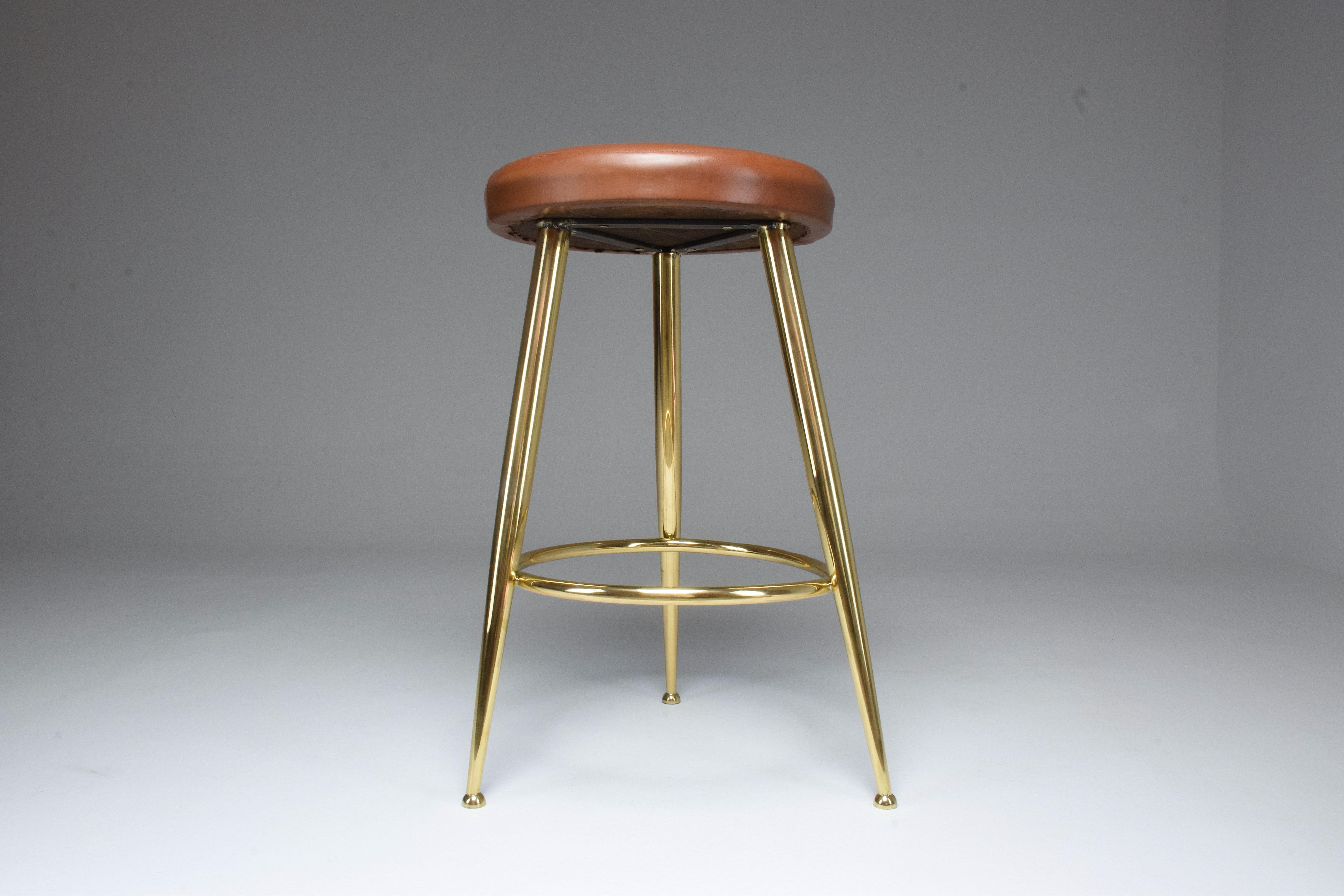 A 20th century vintage stool designed by Italian master Ico Parisi in the 1950s. This piece is highlighted by its solid gold polished brass structure with splayed and tempered legs, which has been re-finished at our atelier, and original light brown