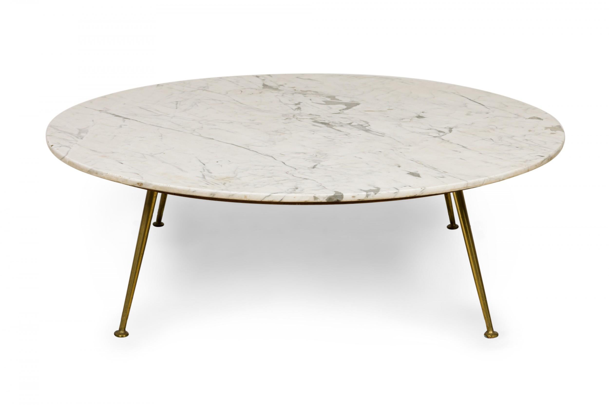 Italian mid-century circular cocktail / coffee table with a Carrera marble top resting on a wooden platform supported by three tapered brass legs ending in circular feet.
 