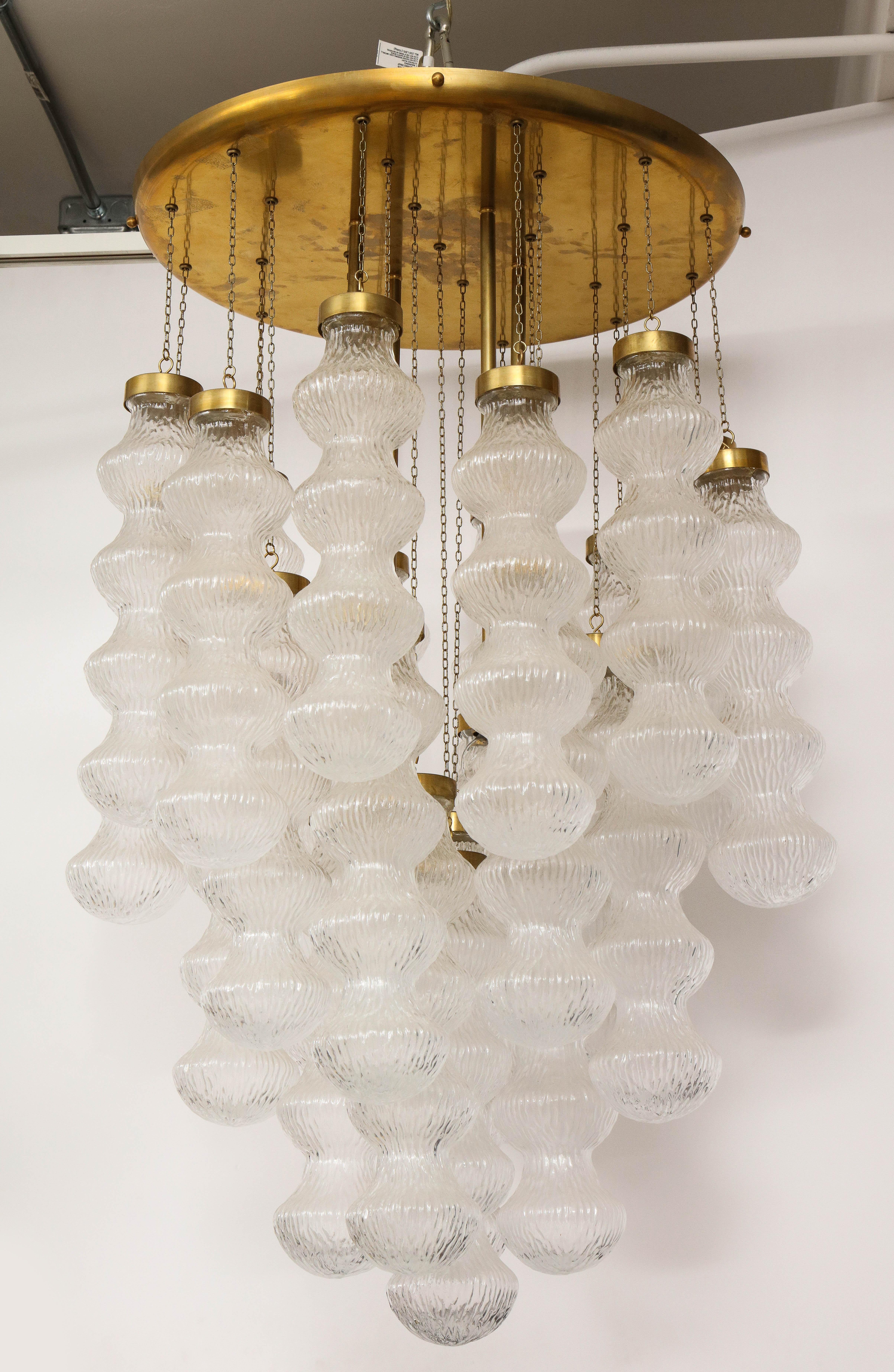 A mid-century Italian four light chandelier attributed to Cenedese comprised of hand blown Murano textured, undulating glass pendants suspended by fine chains of varying lengths from a brass 22.5