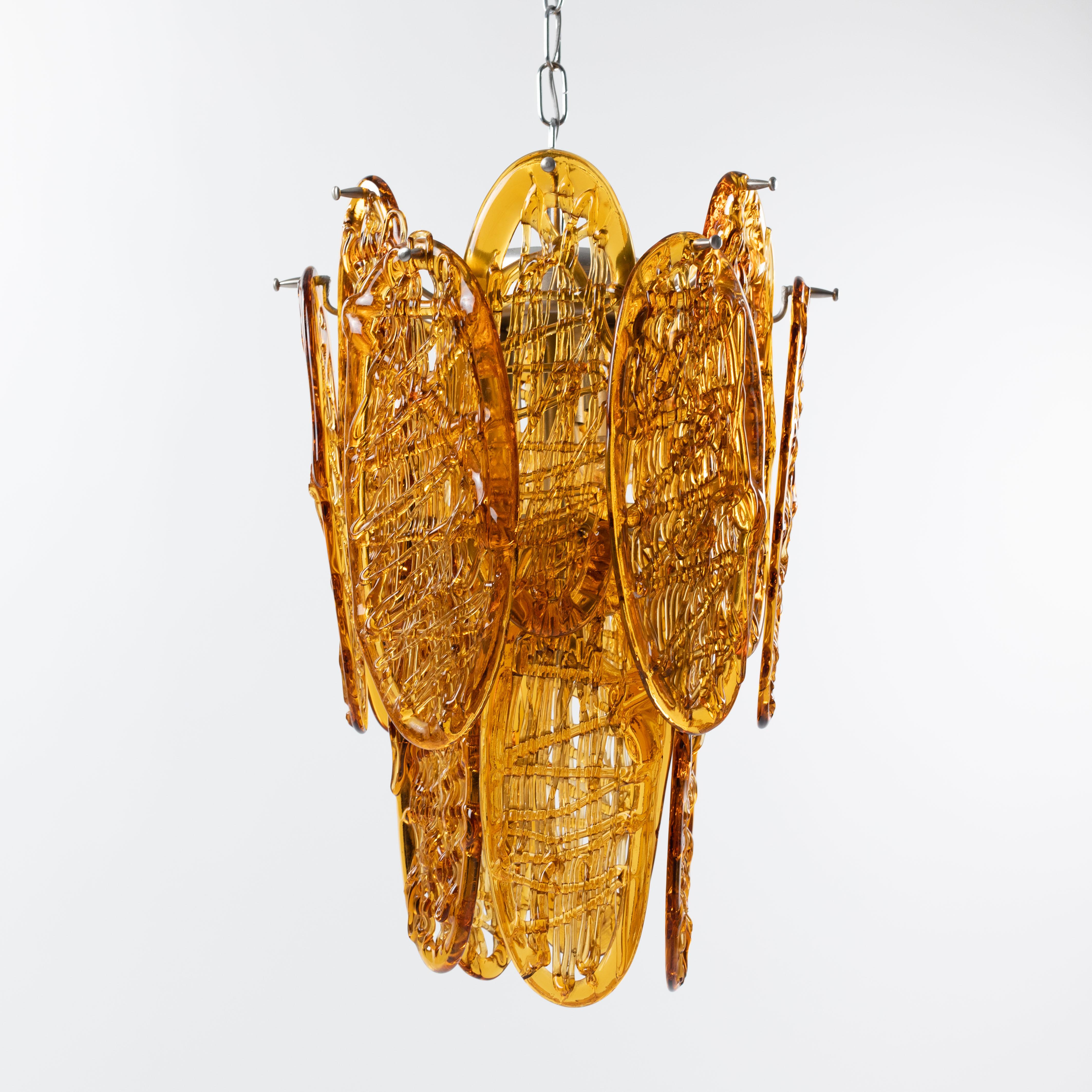 Italian mid-century chandelier manufactured by the company AV MAZZEGA in the 1960s.

17 cognac-coloured, oval Murano glass medallions with a size of 32x12cm form the conical lamp.
The glass medallions are double-storeyed, i.e. staggered, so that