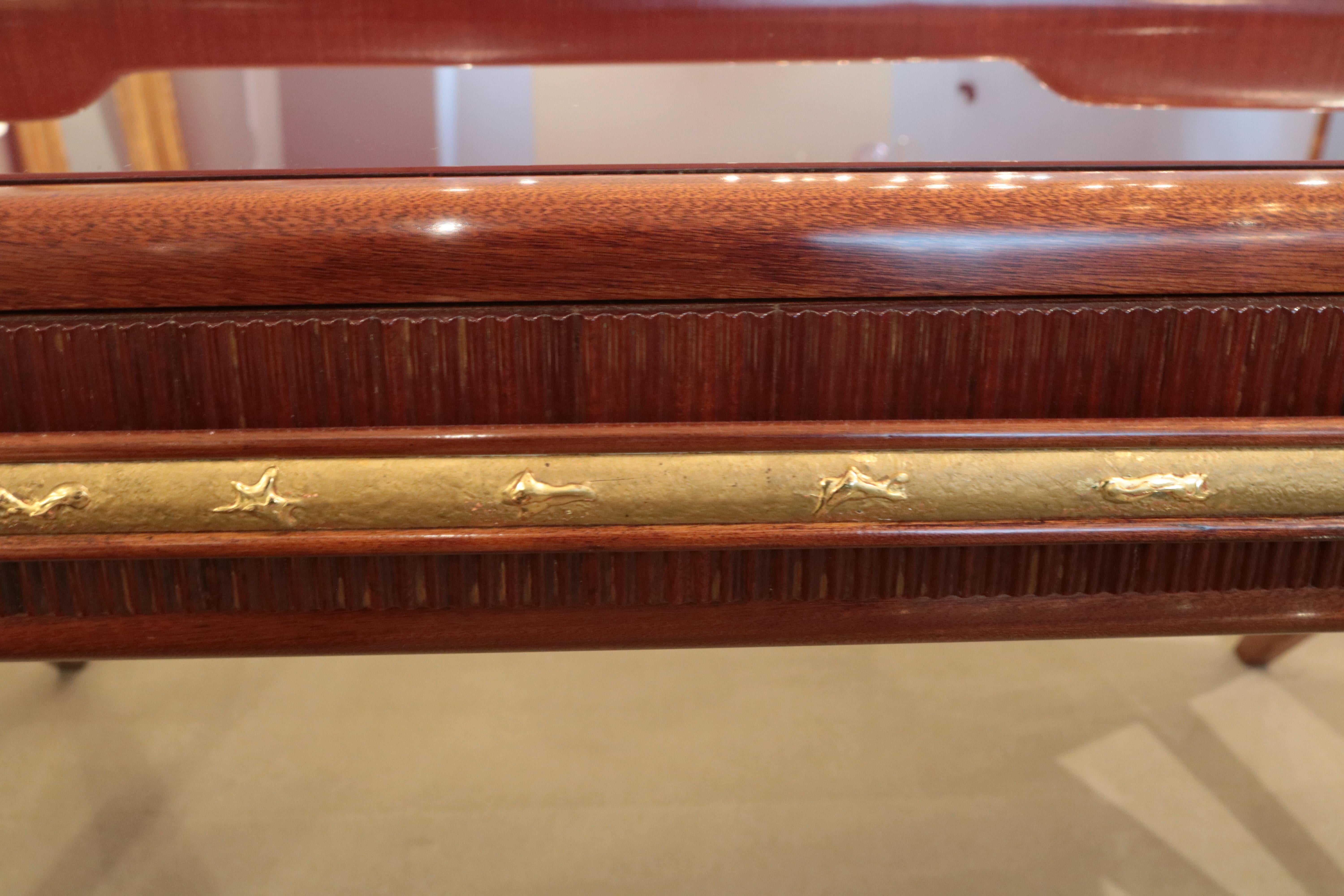 An Italian midcentury console table. 
Mahogany, with patinated brass pulls 
and sabots, carved central gilt drawer pull,
and a glass top.
         