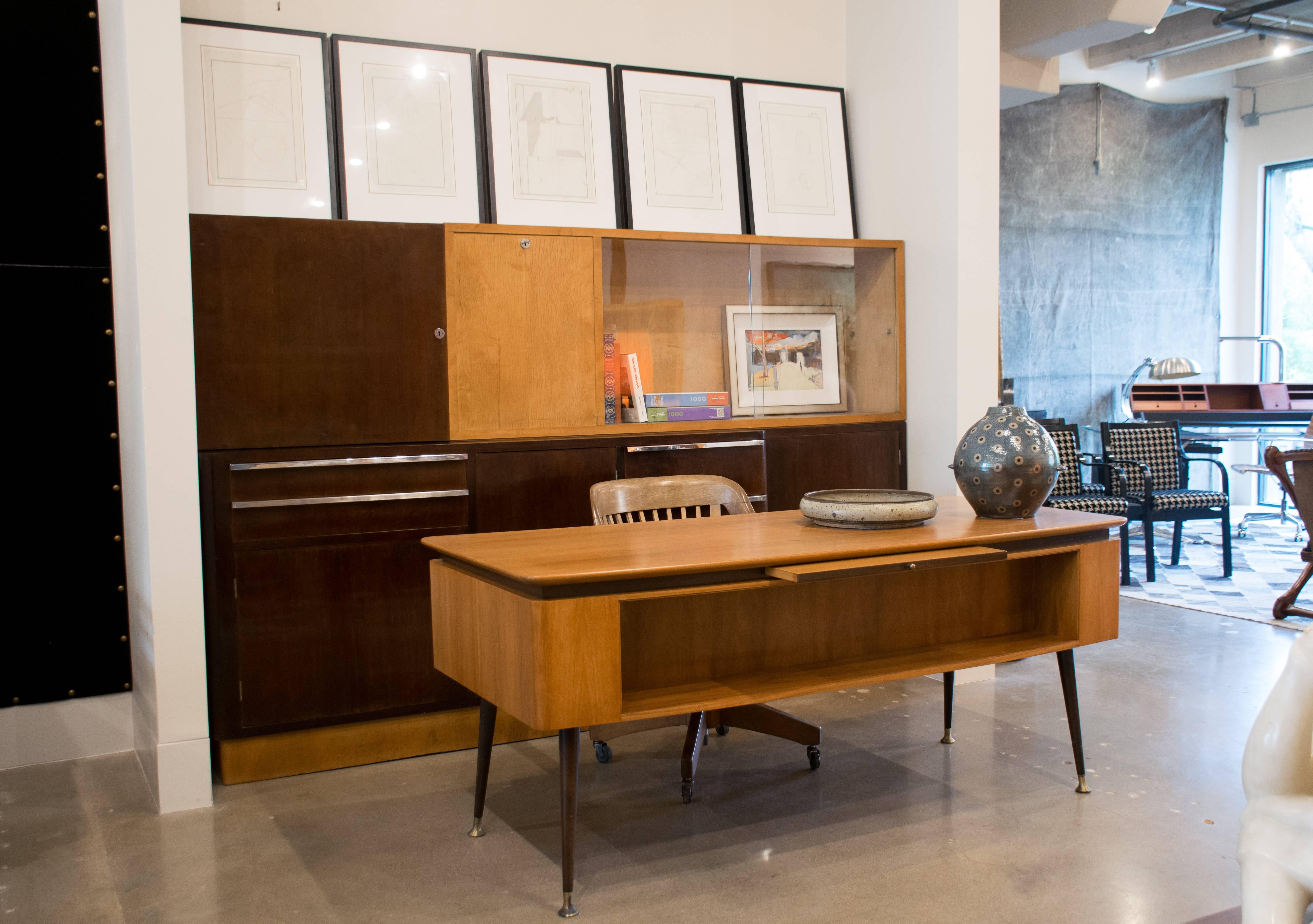 Well proportioned and finely crafted desk of bleached walnut with contrasting dark band and legs. Gently curved top rests above four drawers on one side and pull-out writing surface and book shelf on the other. Elegantly angled legs are capped with