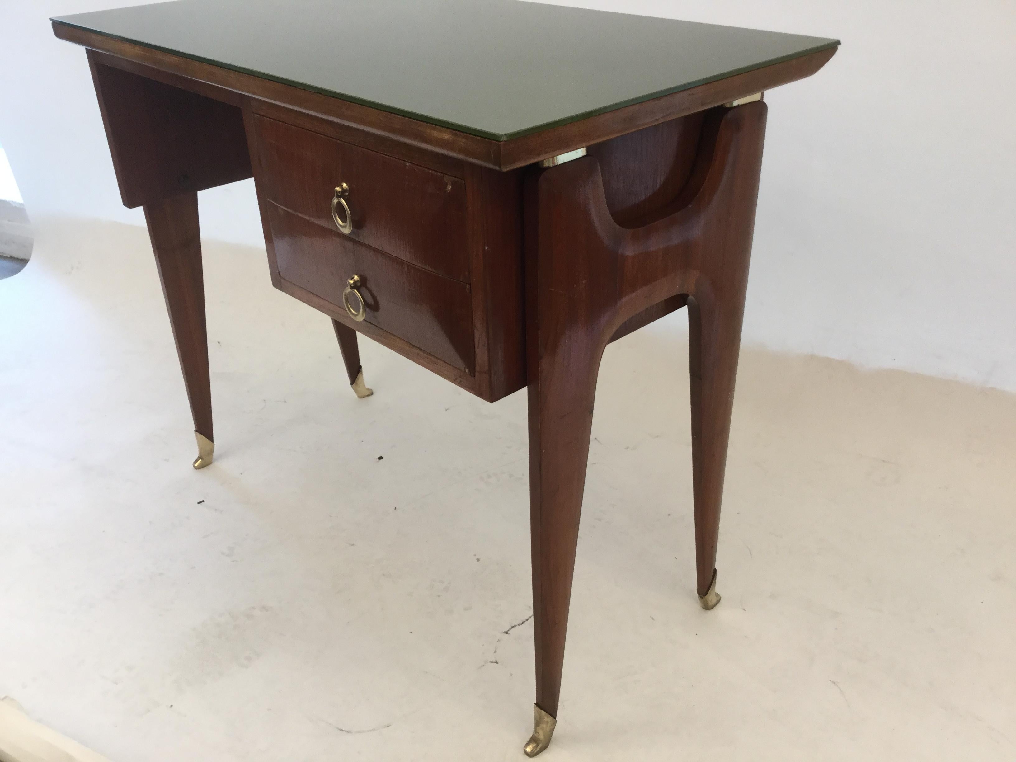 An Italian designed small writing desk executed in fruit wood. Fantastic proportions on sculptural H legs tapering to brass final on the feet. Two drawers with brass hardware with green glass top, Attributed to Carlo De Carli, circa 1950.
In good