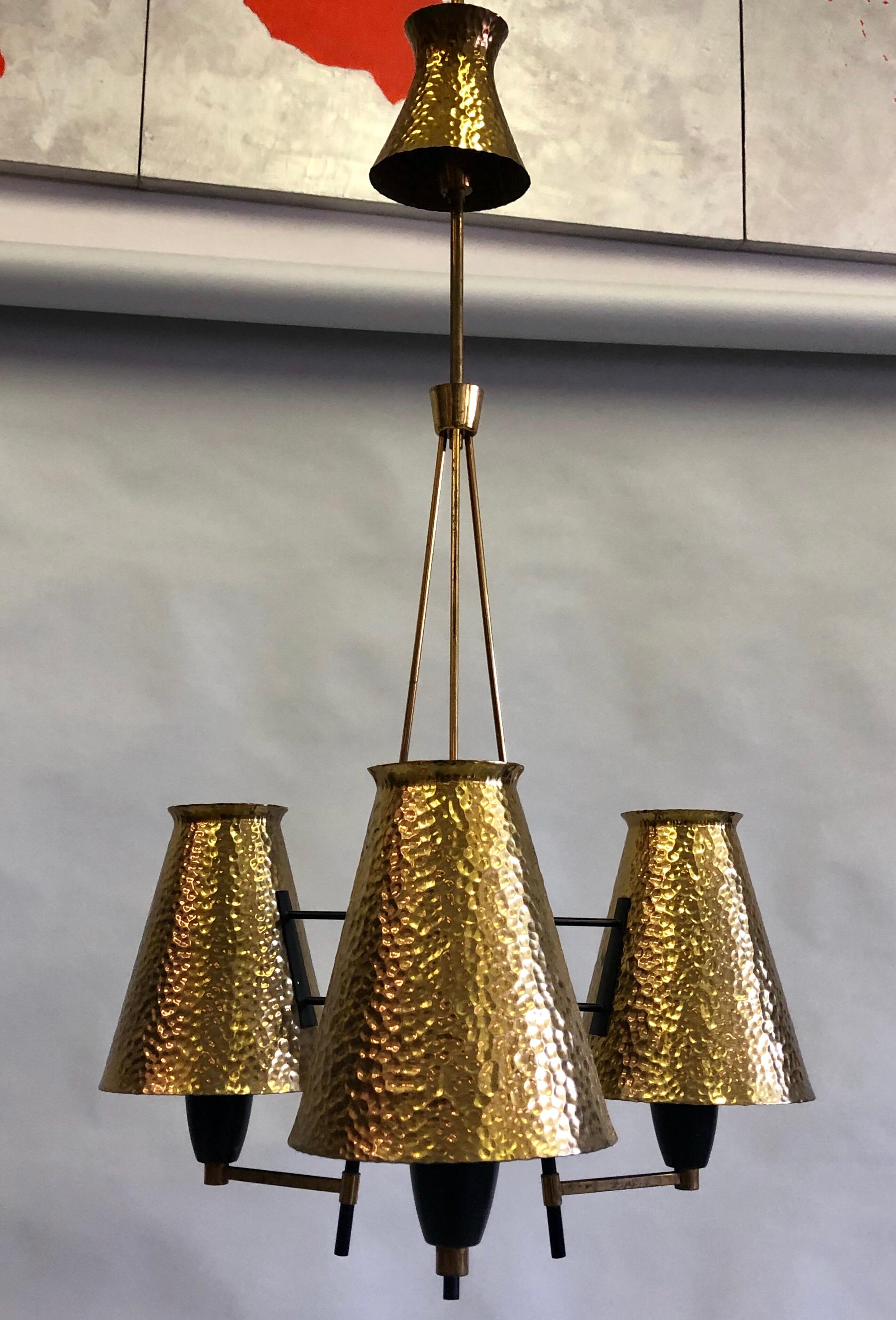 Elegant Italian Mid-Century Modern black enameled metal and hammered brass chandelier by Stilnovo, circa 1948. The pendant features 3 hand-hammered brass reflectors / shades and canopy arranged around a brass and black enameled metal frame. Each
