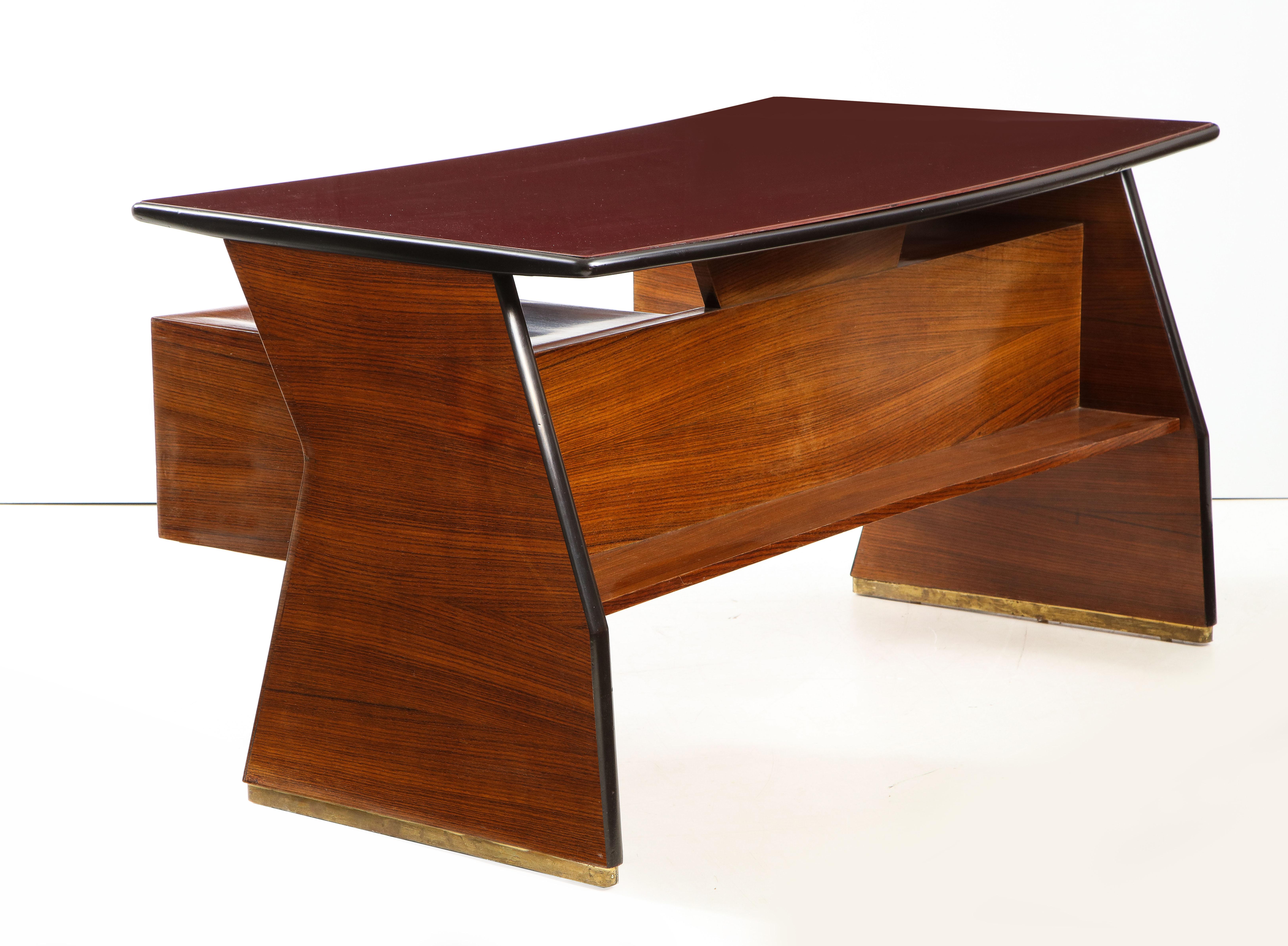 Italian midcentury walnut desk attributed to Vittorio Dassi, the angled brass trimmed sides and shaped top with deep burgundy painted glass over two floating cabinets each with three drawers and brass fluted pulls, the bottom edges trimmed with