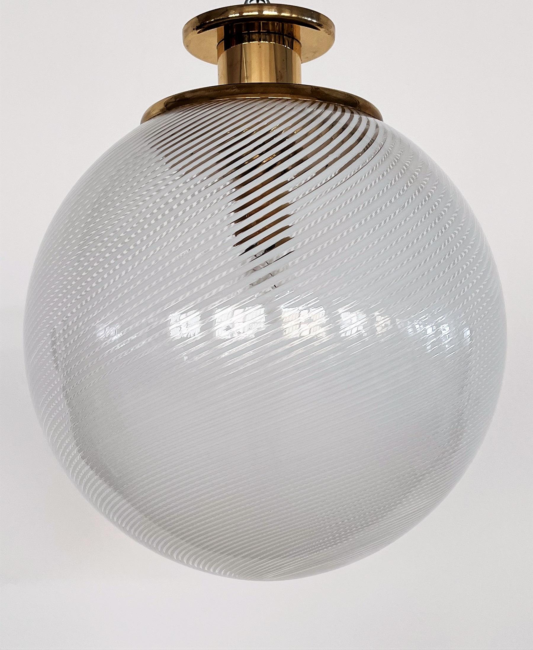 Gorgeous flush mount light or pendant lamp with large murano glass globe and brass frame.
Made in Italy in the 1970s by Venini.
The beautiful glass globe presents shiny white stripes on transparent glass ground. When illuminated, leaves gorgeous