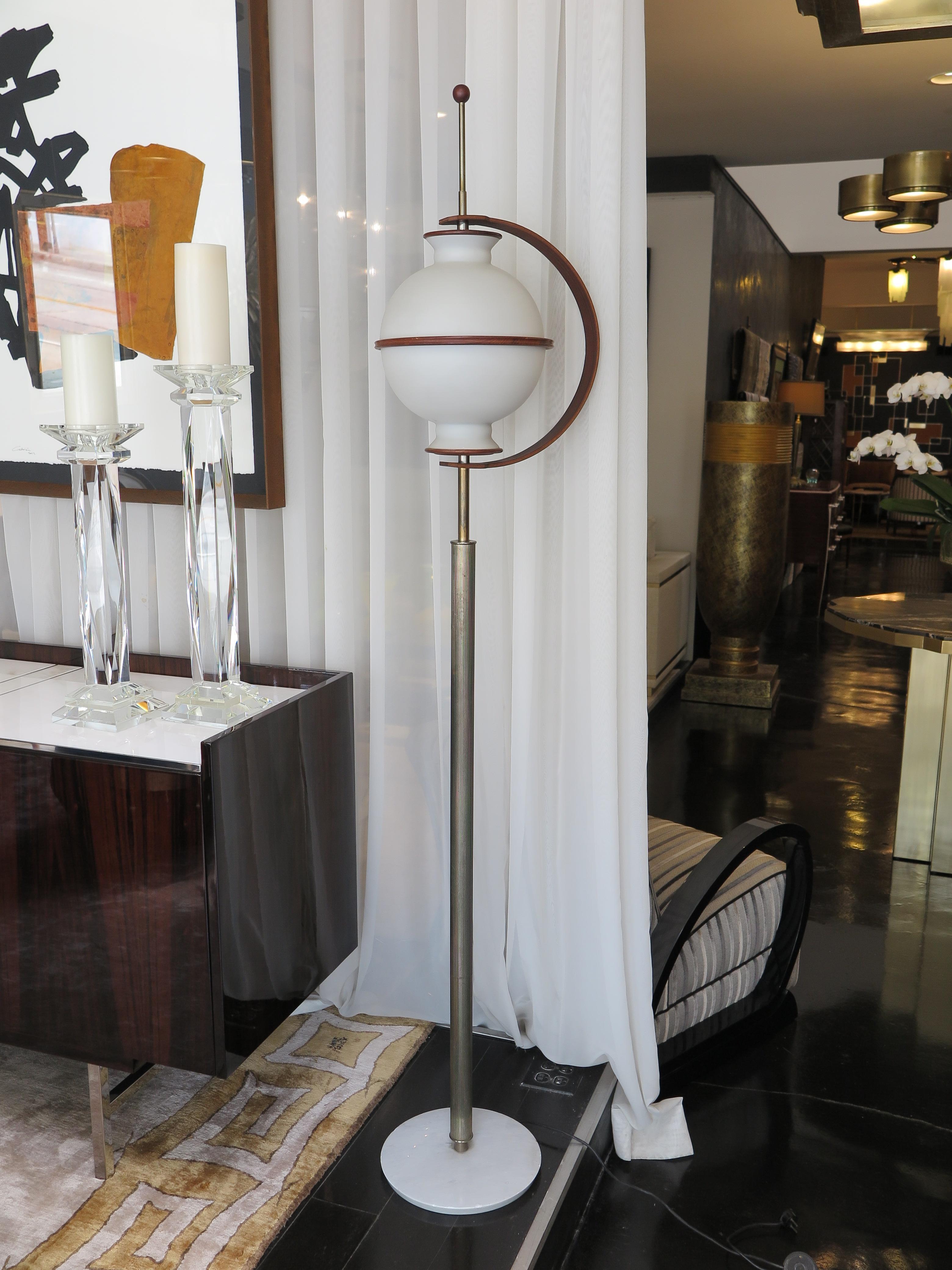 This unusual floor lamp evokes a futuristic aesthetic. Round globe shade in frosted milk glass and framed in a curved wooden arm in rosewood. The ribbed brass stem leads to a round white marble base. This piece feature 3 bulbs inside.