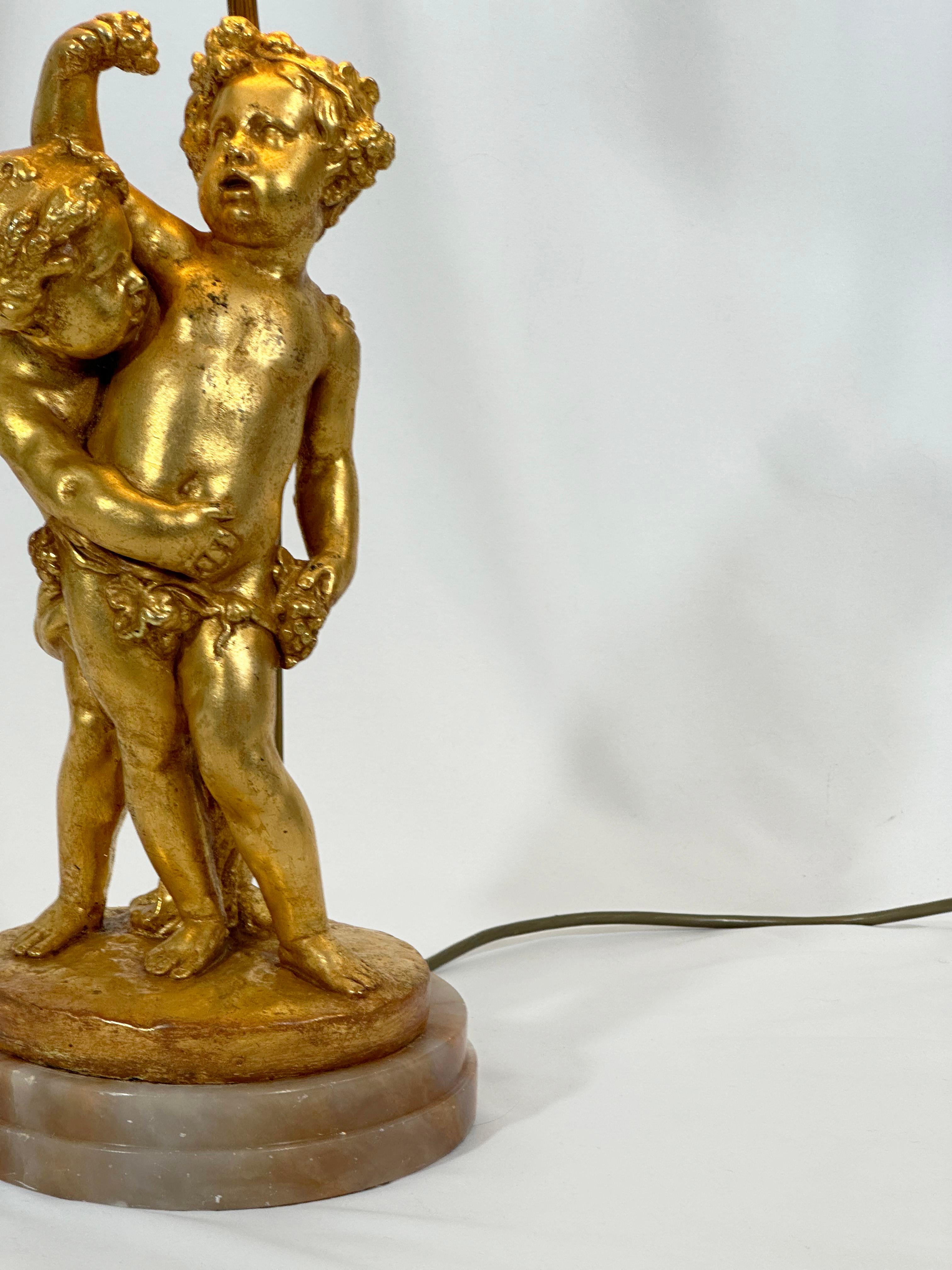 Crafted in Italy’s post-war design renaissance, this gilded table lamp marries the playful charm of putti—cherubic figures drawn from the artistic wells of Renaissance and Rococo—with the grandeur of mid-century aesthetics. The centrepiece, a