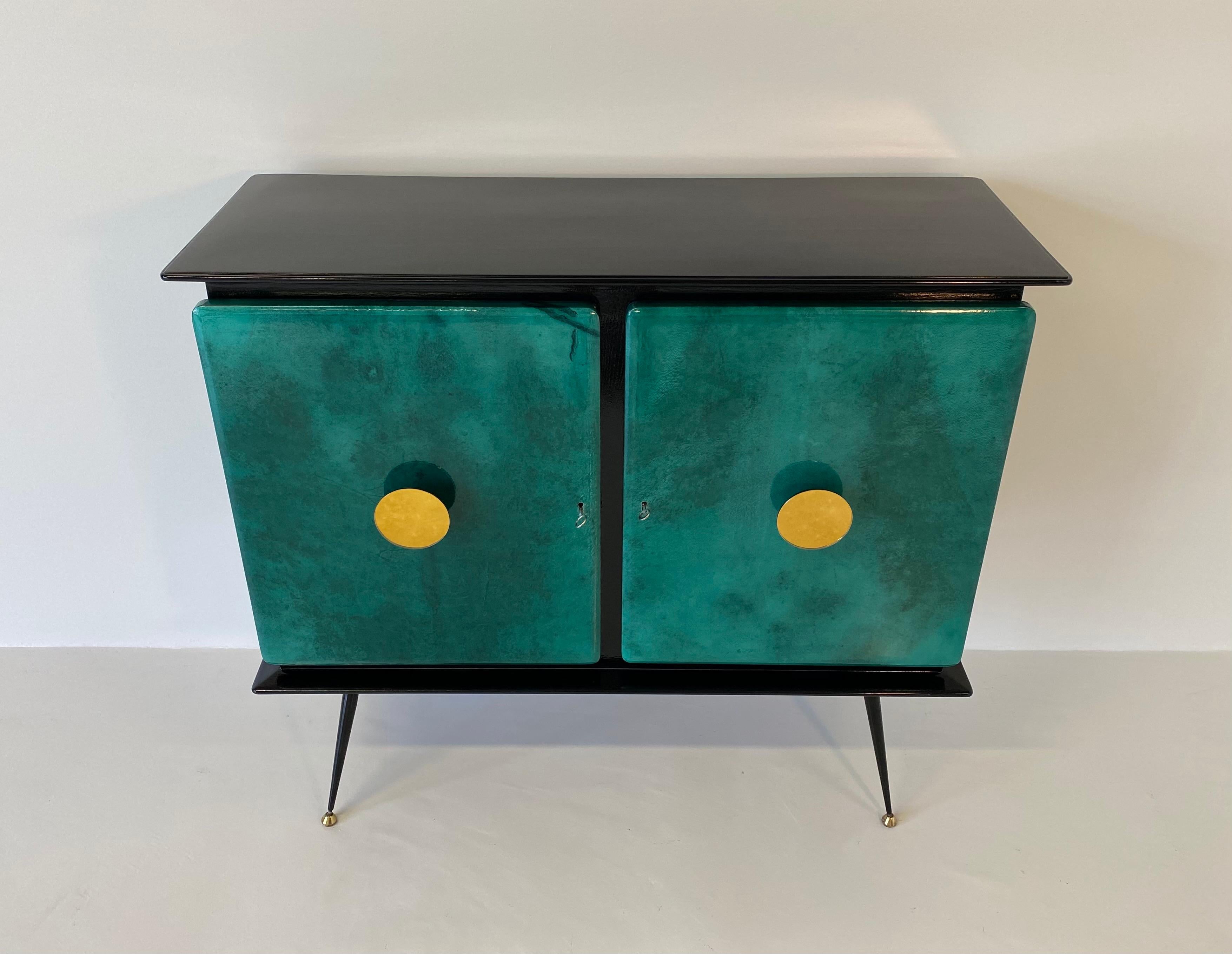 This mid-century bar cabinet was produced in the 1950s in Italy.
It is completely black lacquered with green parchment doors.
The handles are in gold mirror and the feet are in metal and brass.
The internal drawers are in maple while the