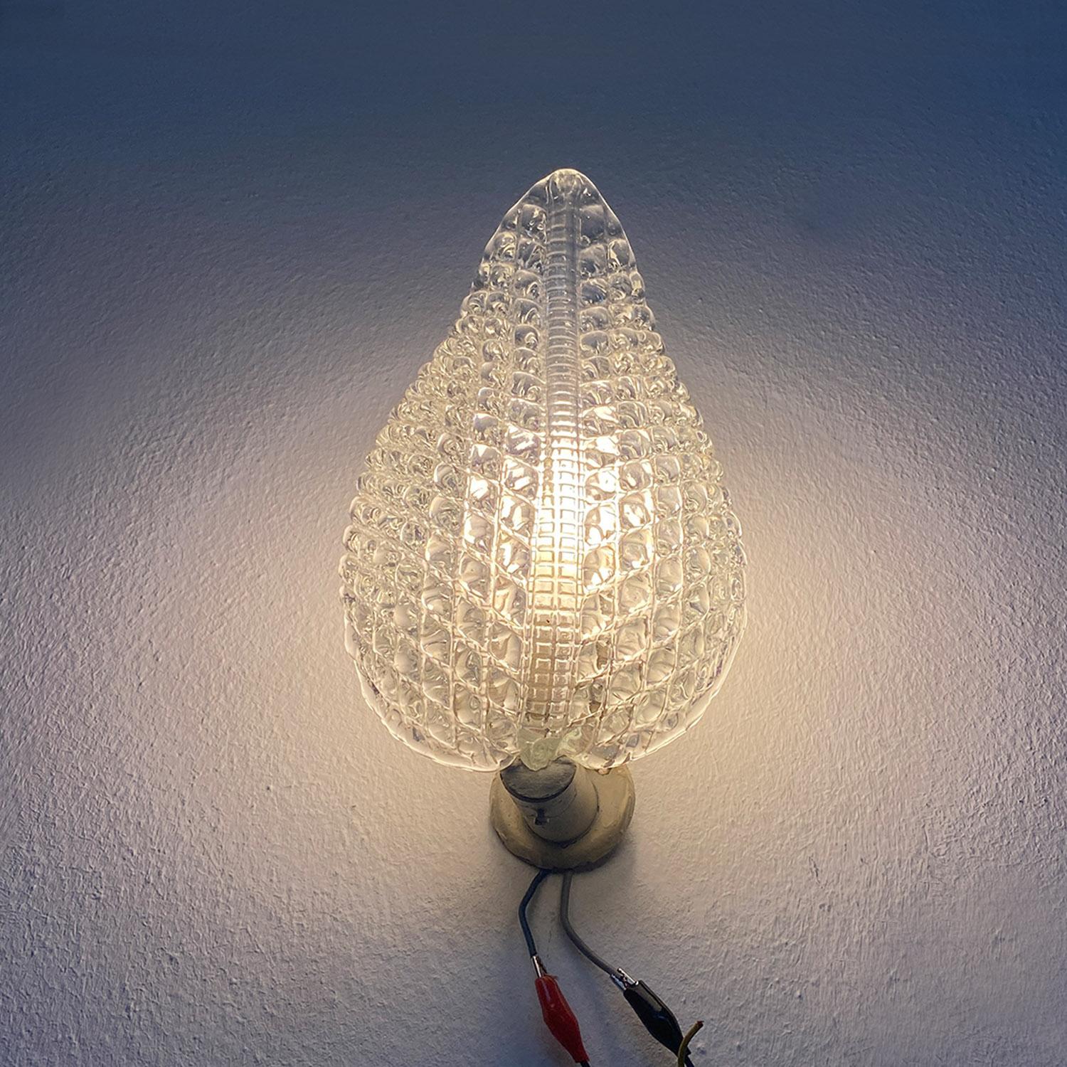 Aplique italiano de mediados de siglo con soporte metálico y cristal en forma de hoja, años 50.
Aplique con soporte metálico de pared, sobre el que se coloca el portalámparas con conexión E14 y al que también se ancla el cristal impreso en forma de