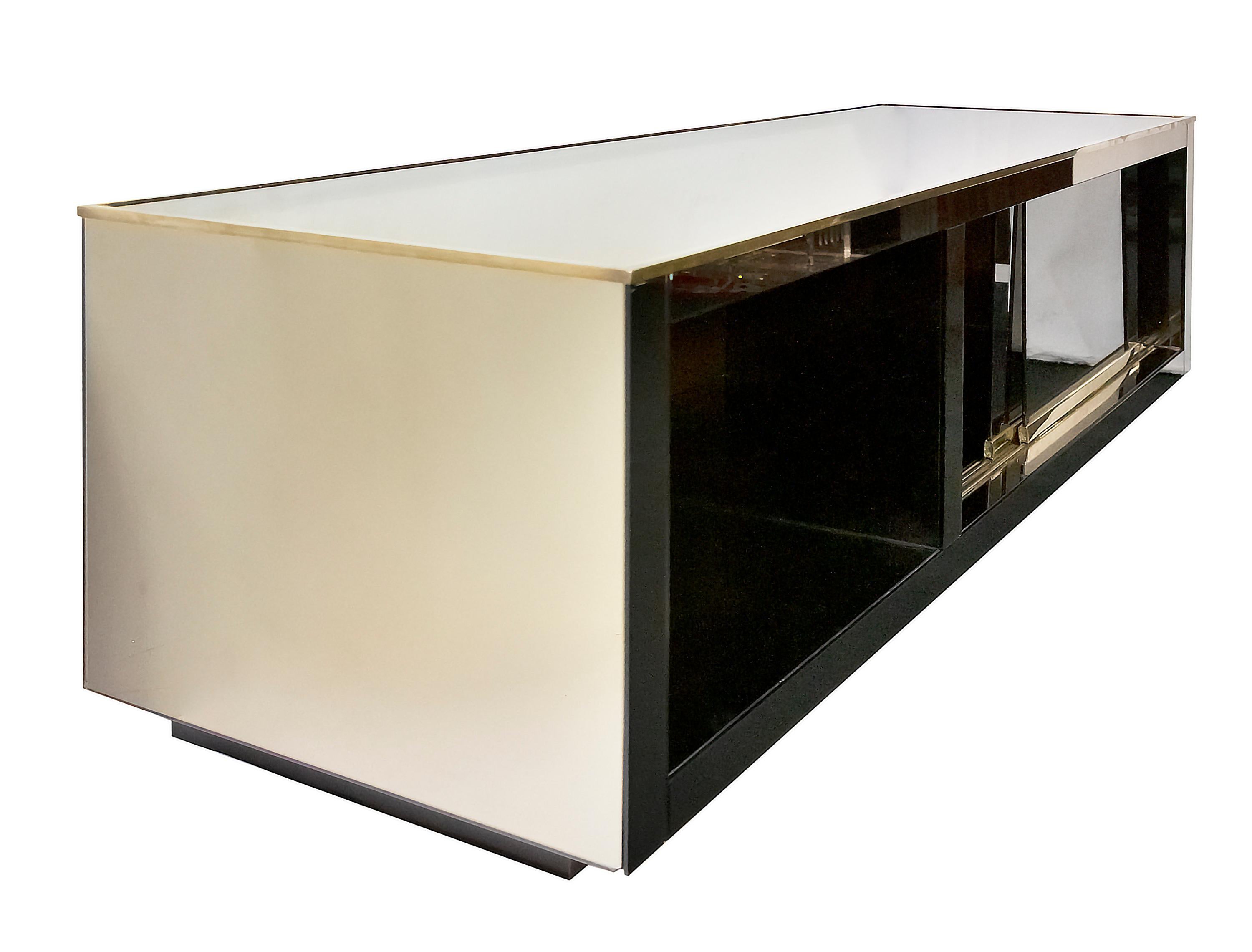 Italian mid-century mirrored sideboard or console stand for television in the style of Romeo Rega. This furniture is all decorated with mirror, open shelve storage and closed part with two sliding doors with brass decor elements.
Overall very