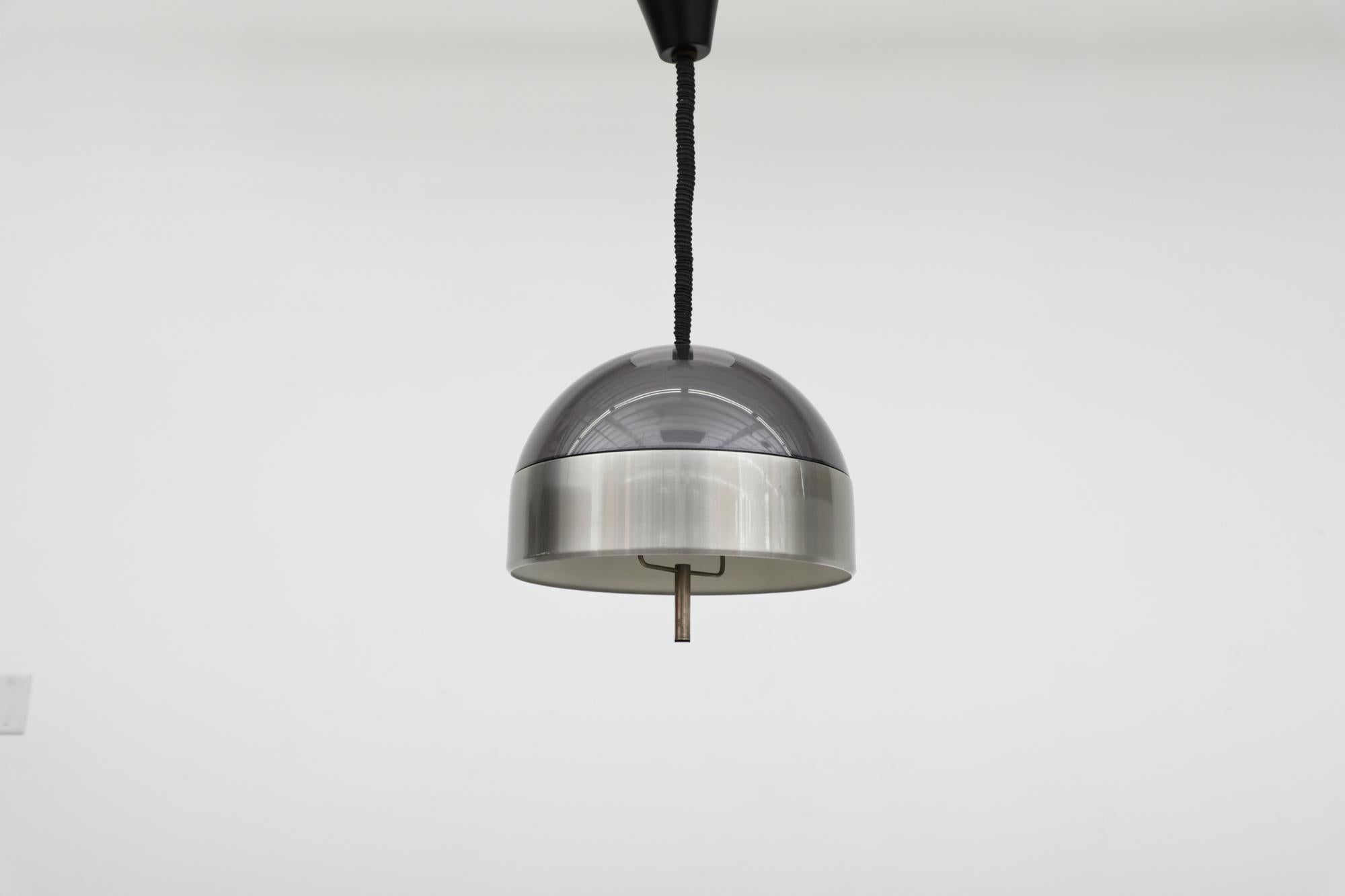 Incredibile ciondolo a cupola MOD 1970 regolabile in altezza con guscio in plexiglass fumé, cintura in alluminio spazzolato e maniglia in metallo. Si può tirare delicatamente la maniglia per abbassare e alzare l'altezza della luce.  In condizioni