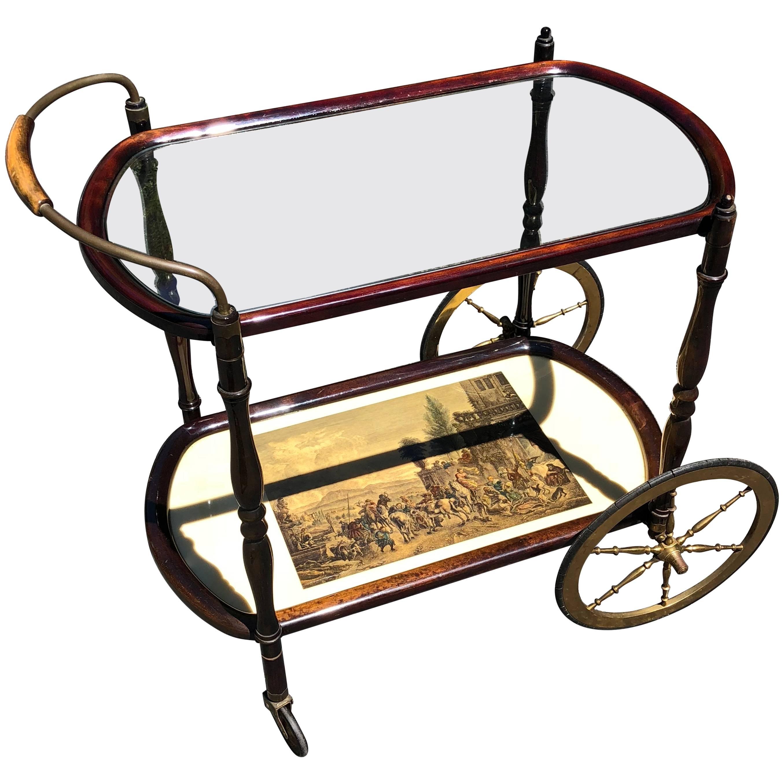 Cesare Lacca style Italian Mid-Century Modern bar cart.
This cart is a real beauty. The frame is a rich deep wood. The top tier is glass and the lower second tier painting of Italian scene. The original casters and large wheels are slender and